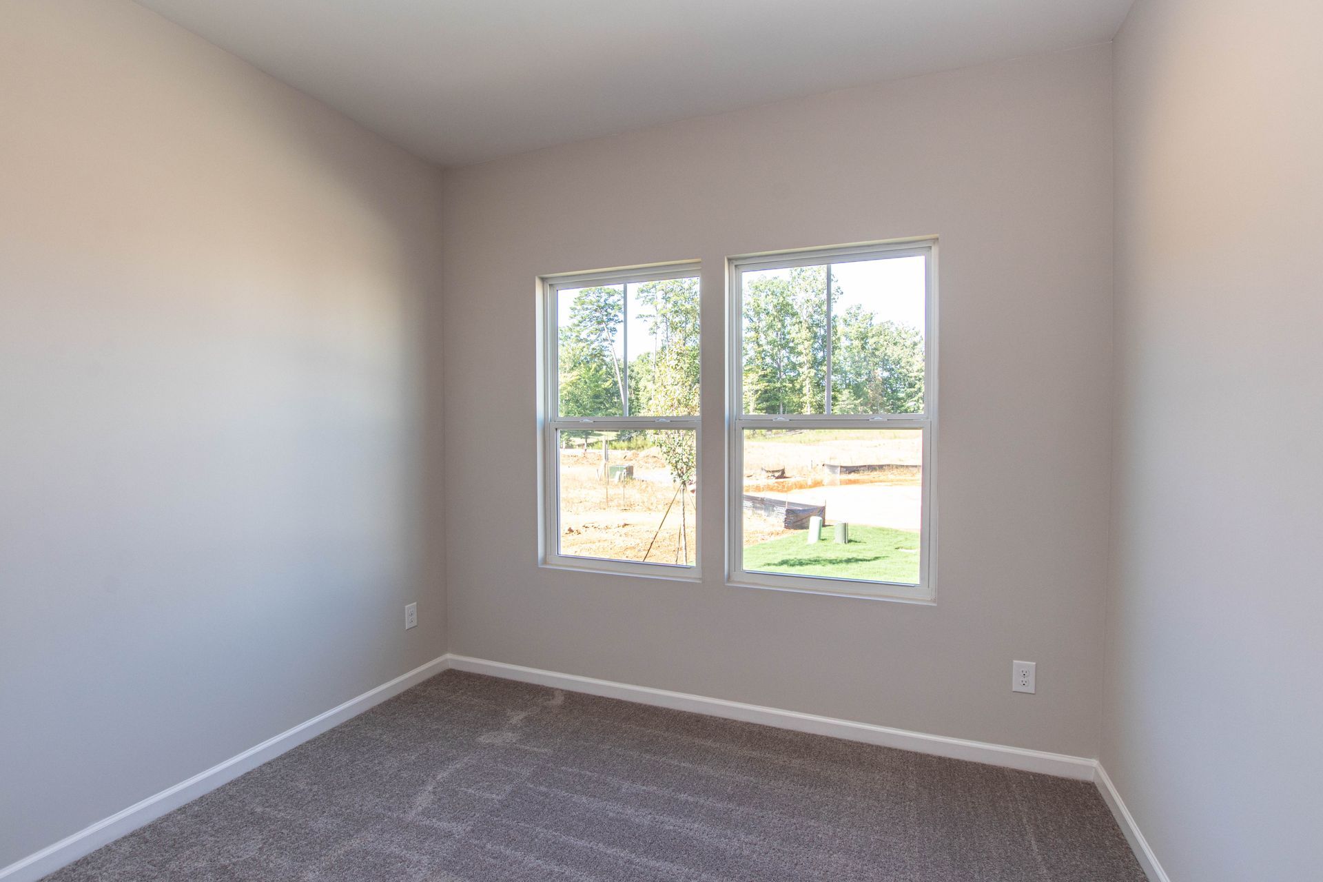 An empty bedroom with two windows and a carpeted floor.