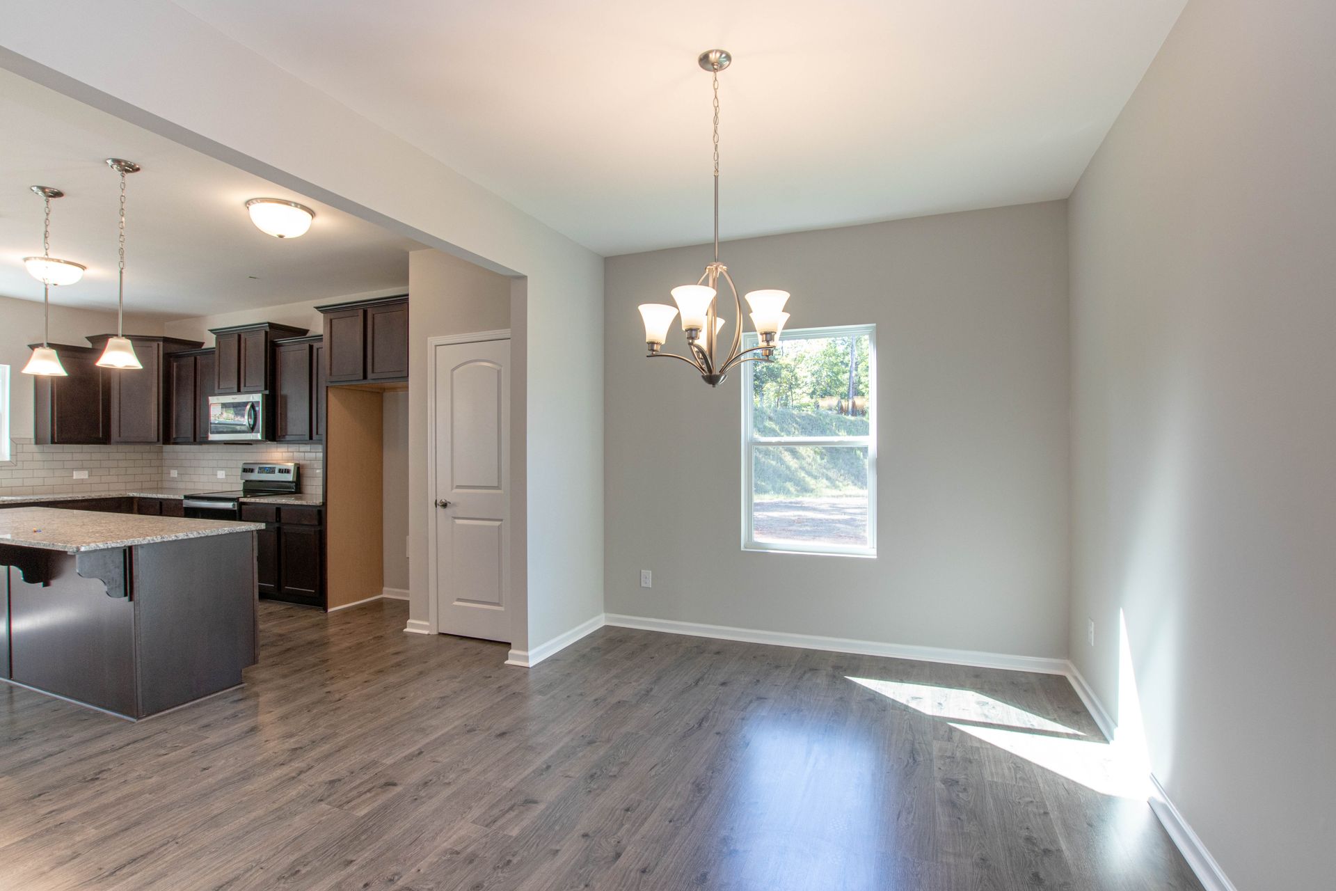 An empty living room with hardwood floors and a chandelier hanging from the ceiling.