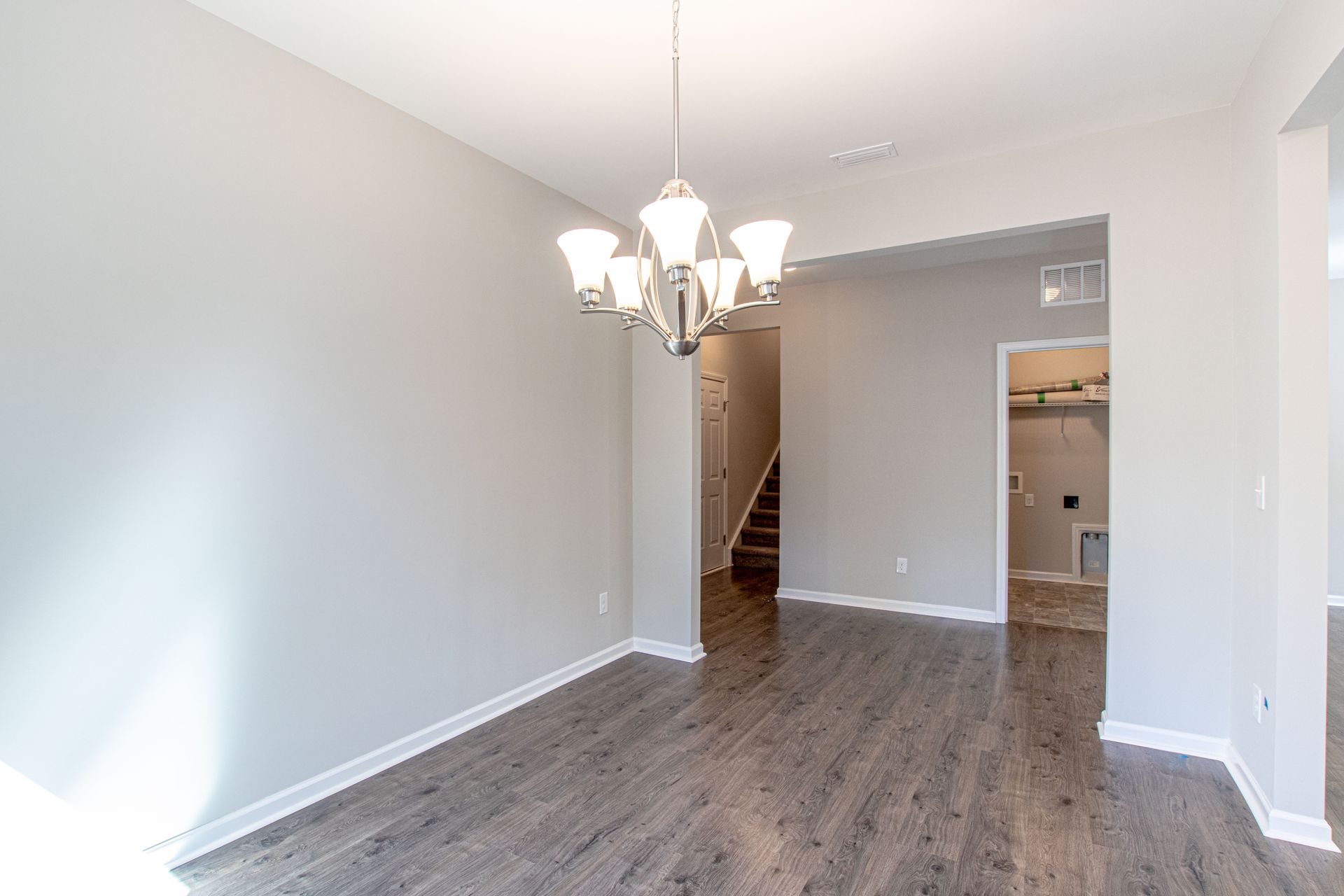 An empty dining room with hardwood floors and a chandelier.
