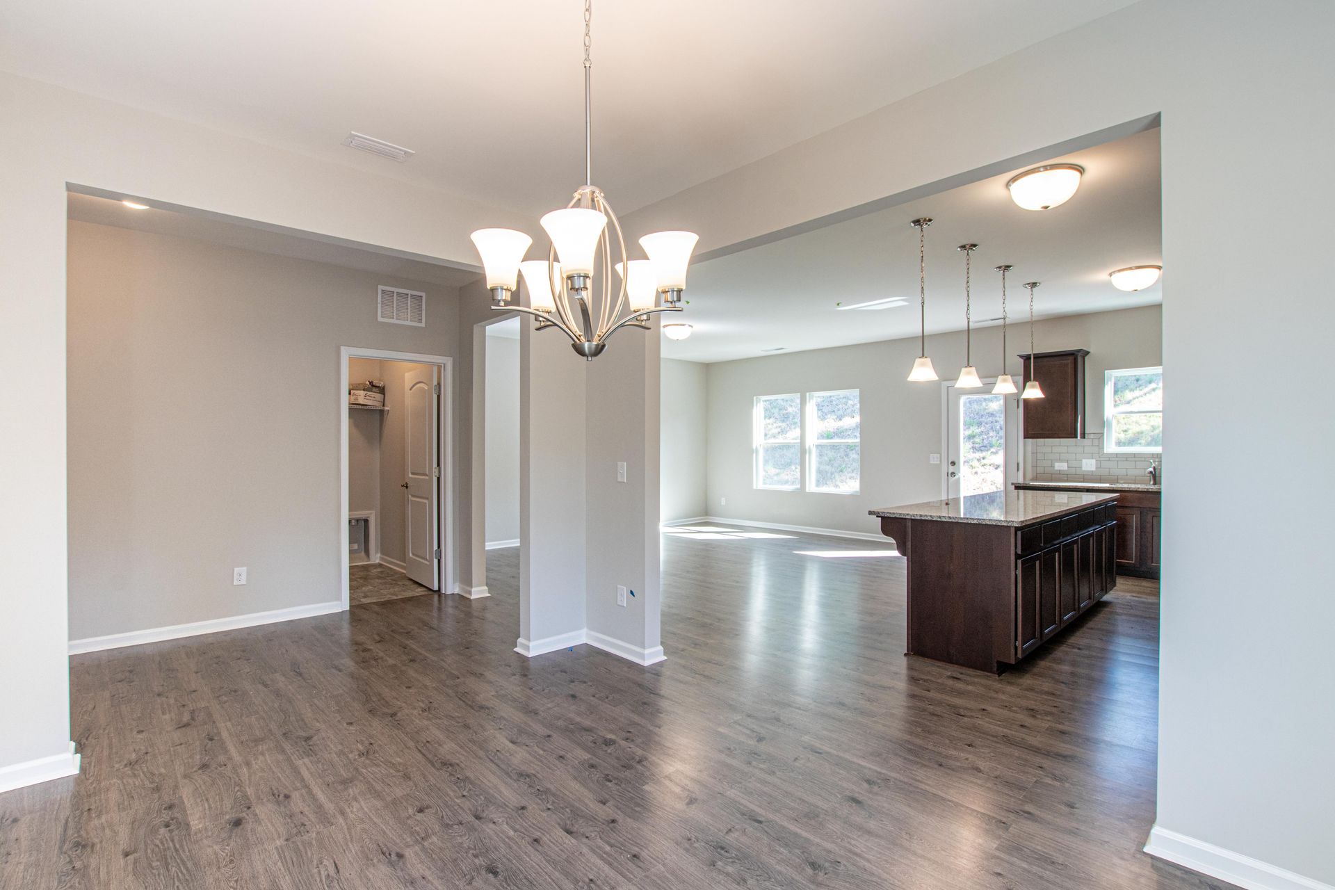 An empty house with hardwood floors and a chandelier hanging from the ceiling.