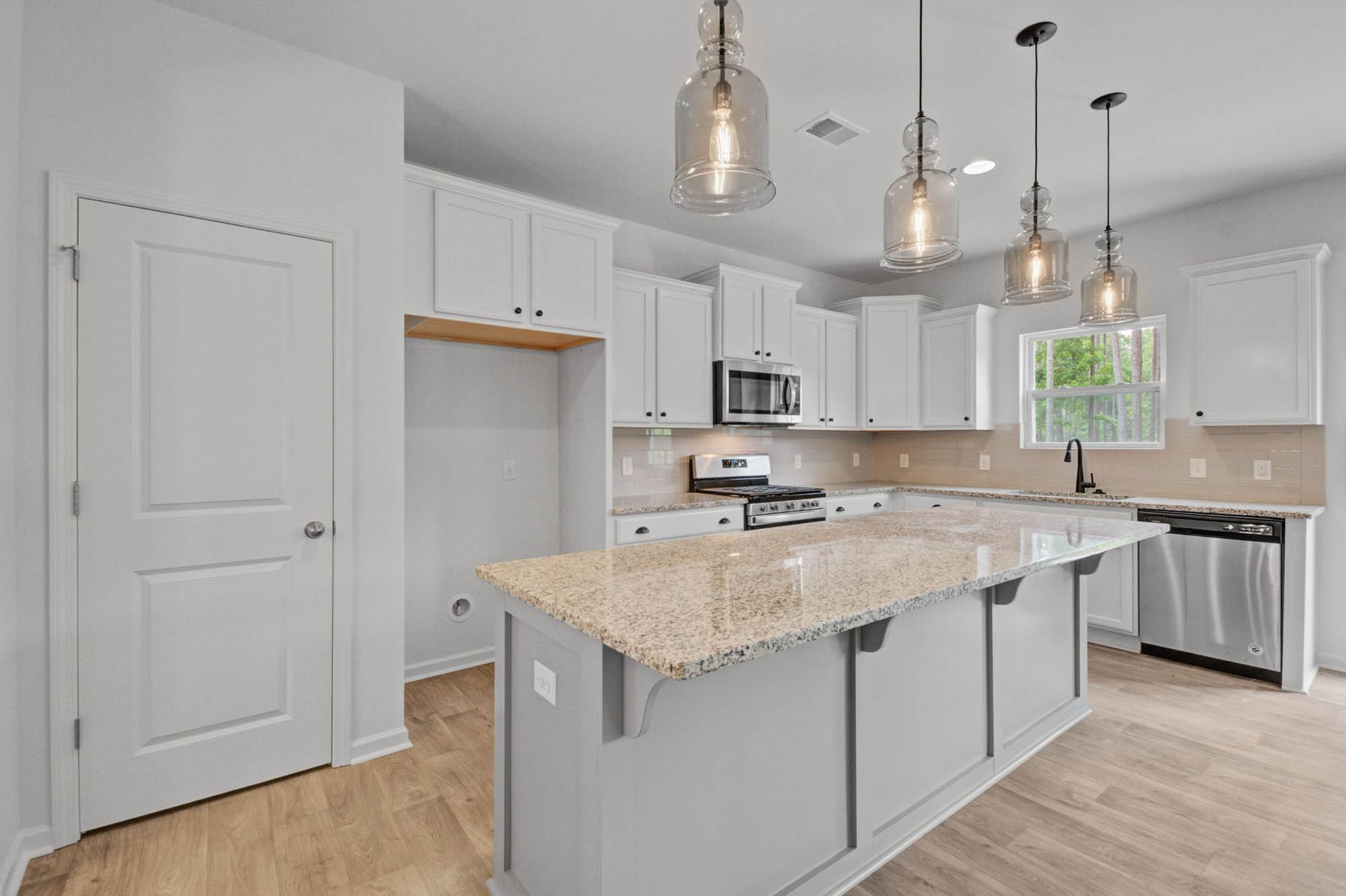 A kitchen with white cabinets , granite counter tops , stainless steel appliances and a large island.
