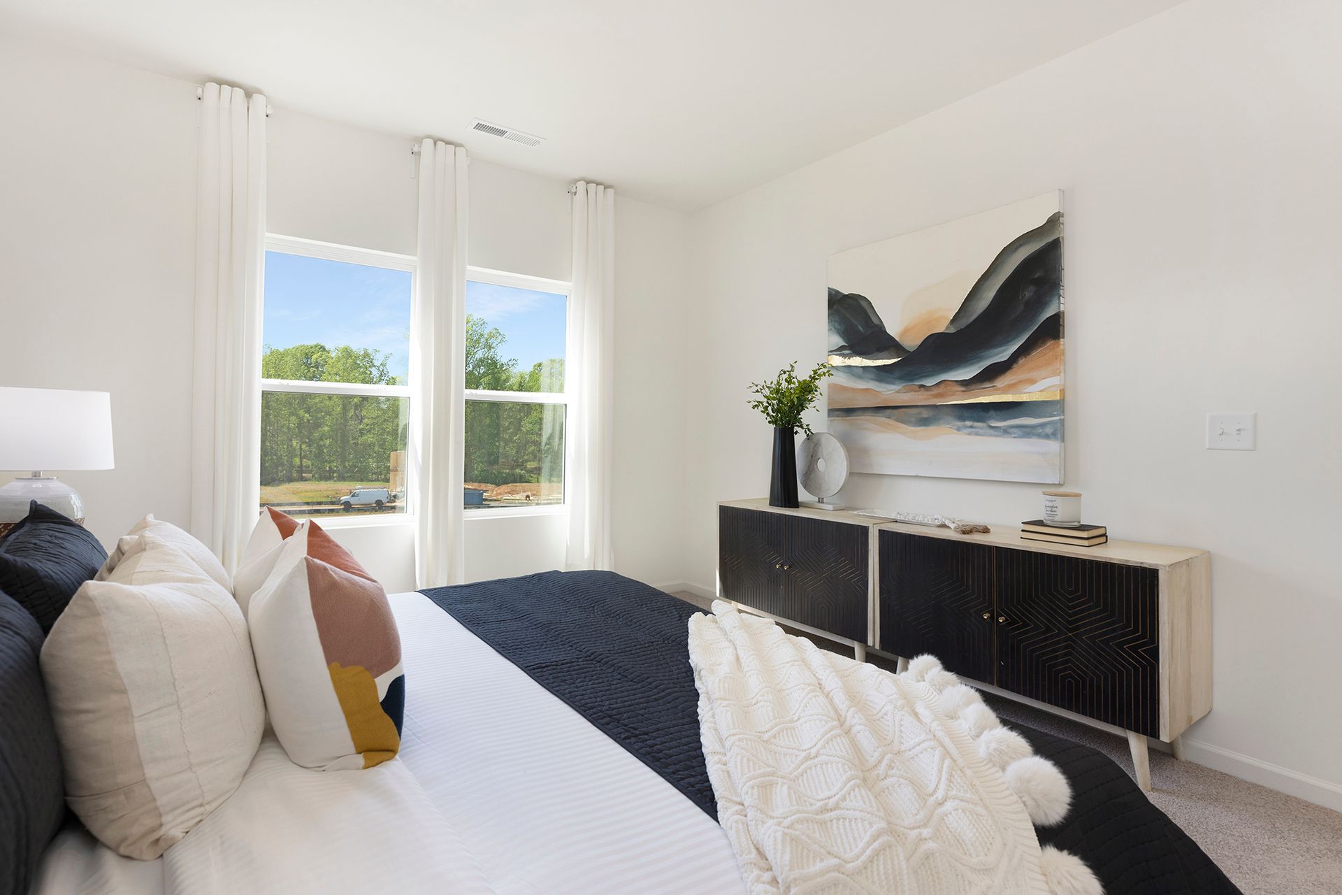 A bedroom with a large bed , dresser , and two windows.