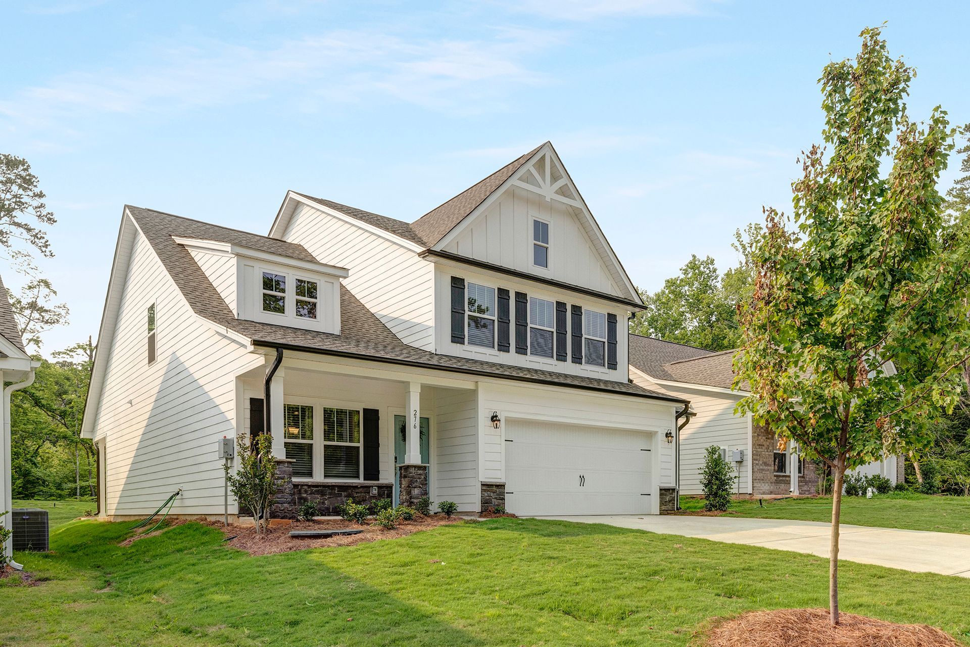 A large white house with a large garage and a tree in front of it.