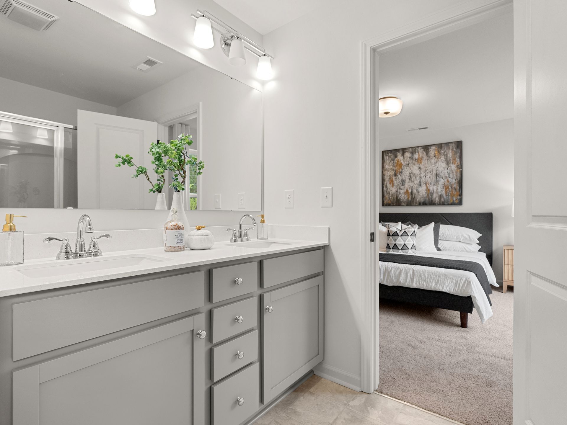 A bathroom with two sinks and a large mirror leading to a bedroom.