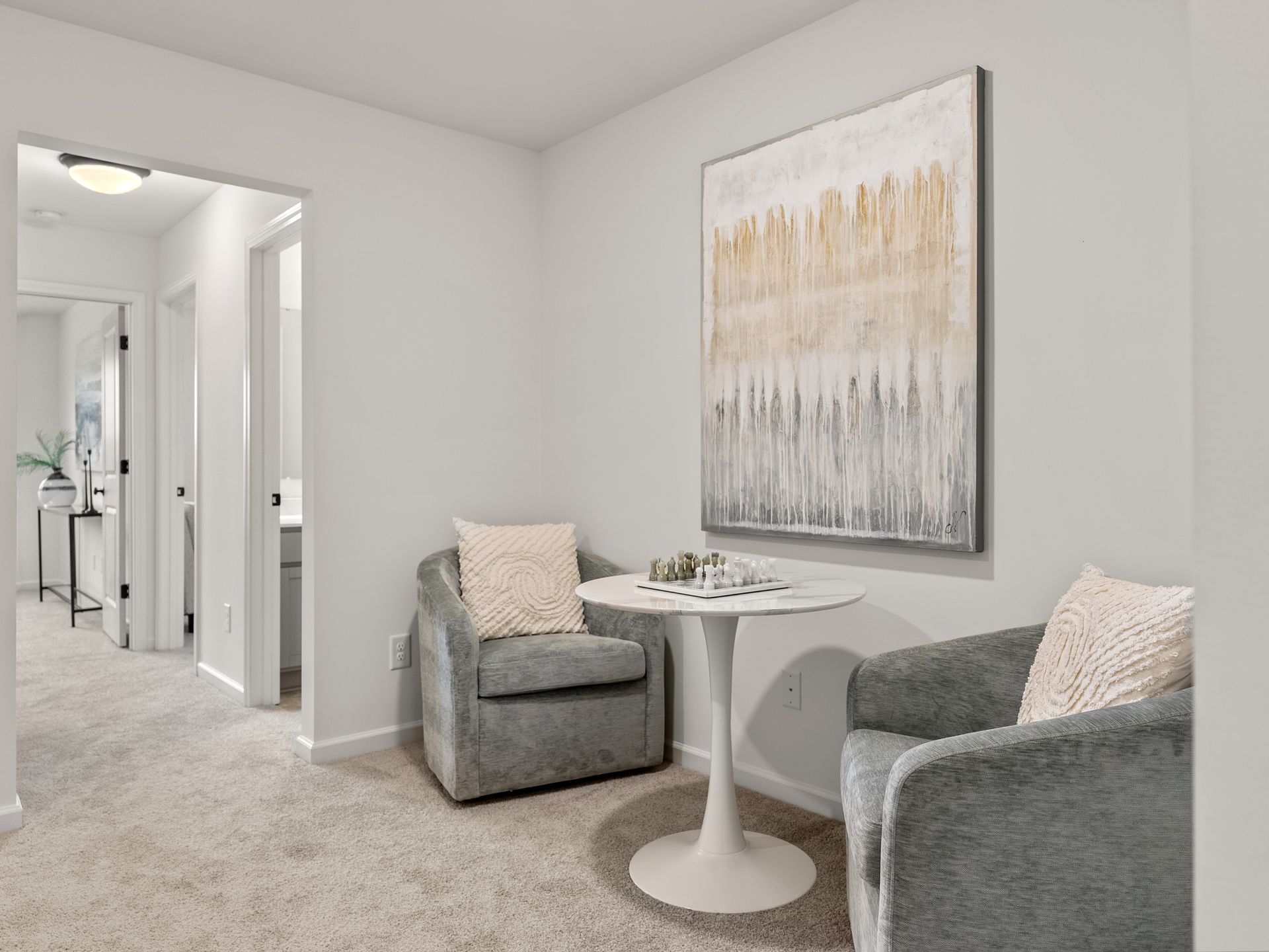 A living room with two chairs , a table and a painting on the wall.