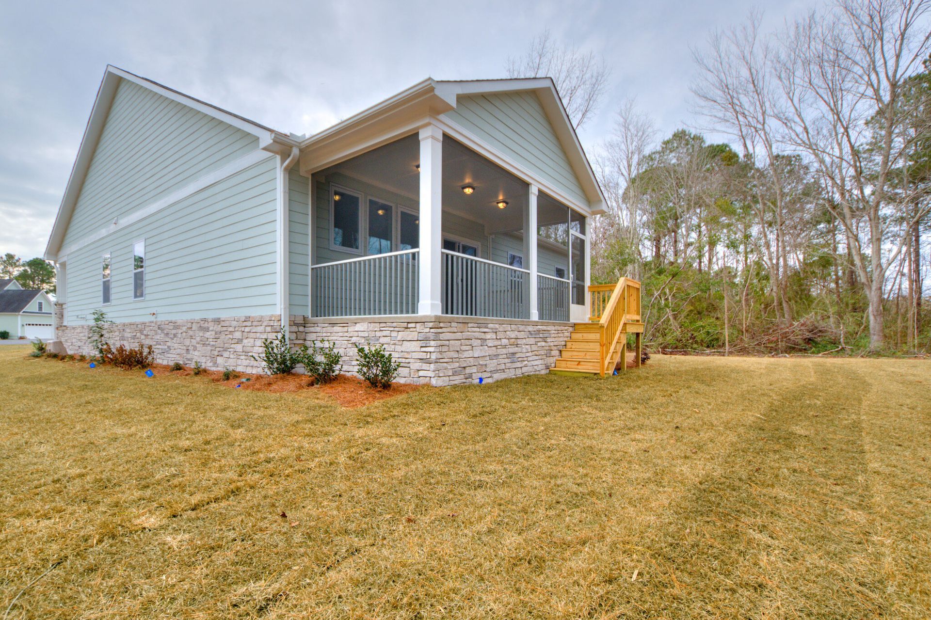 A house with a porch and stairs is sitting on top of a lush green field.