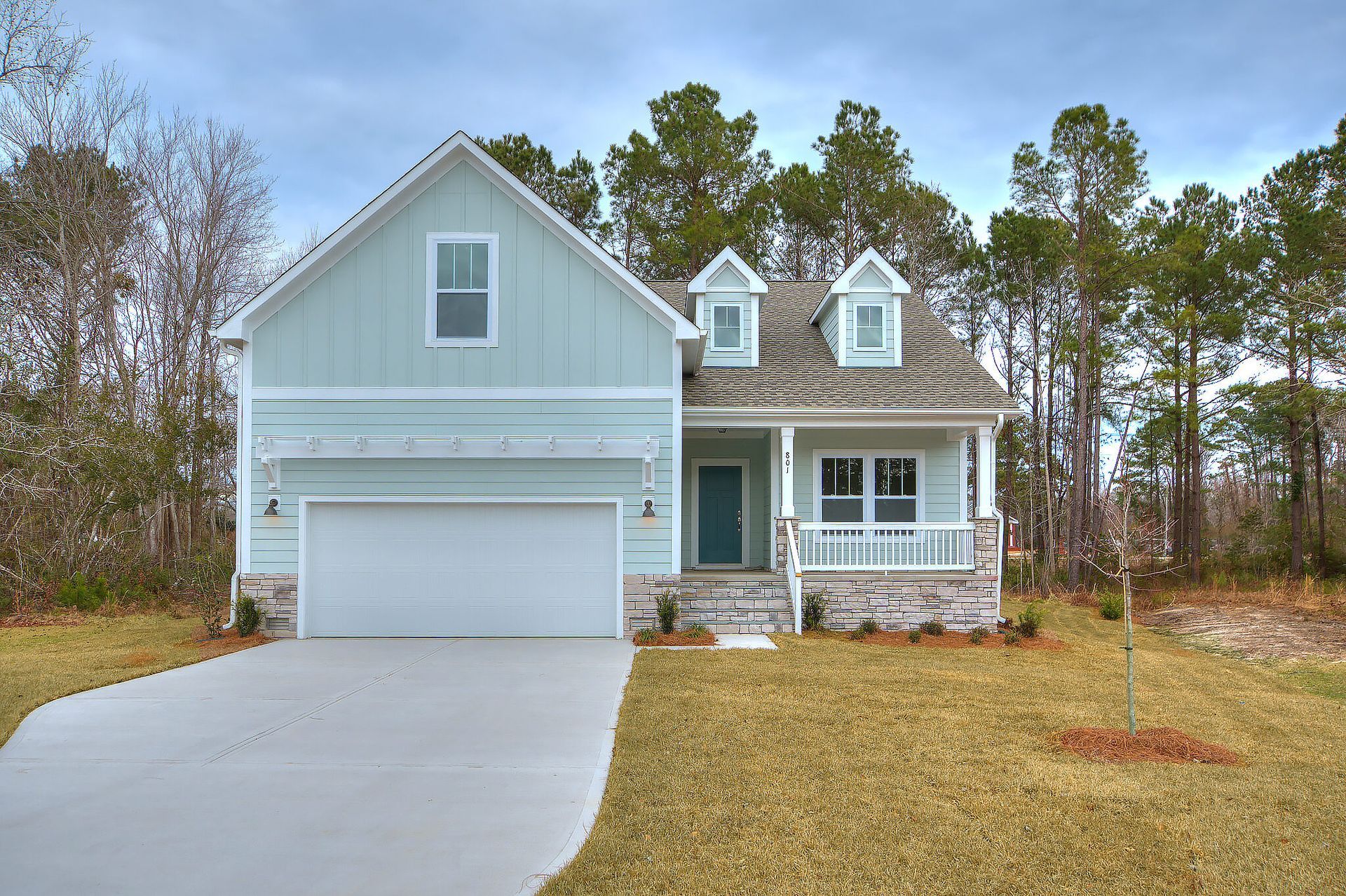 A blue and white house with a garage and a porch surrounded by trees.
