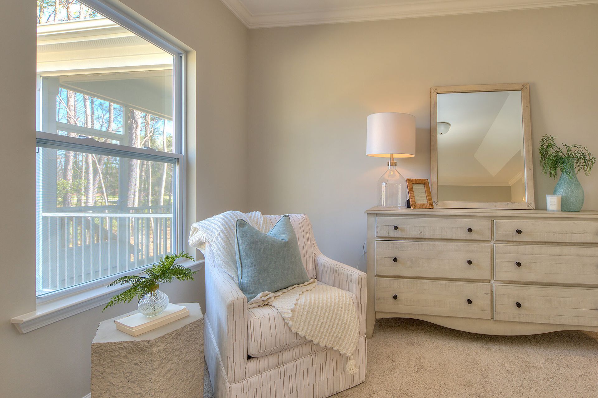 A bedroom with a chair , dresser , mirror and window.