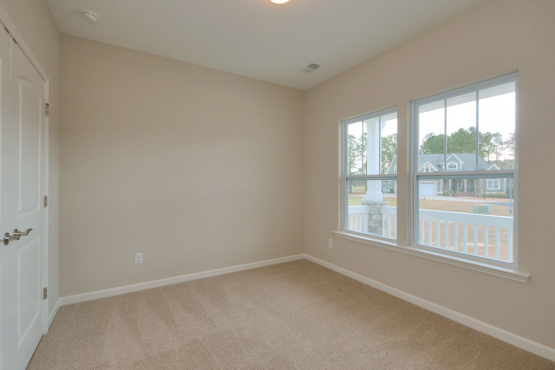 An empty bedroom with two windows and a carpeted floor.