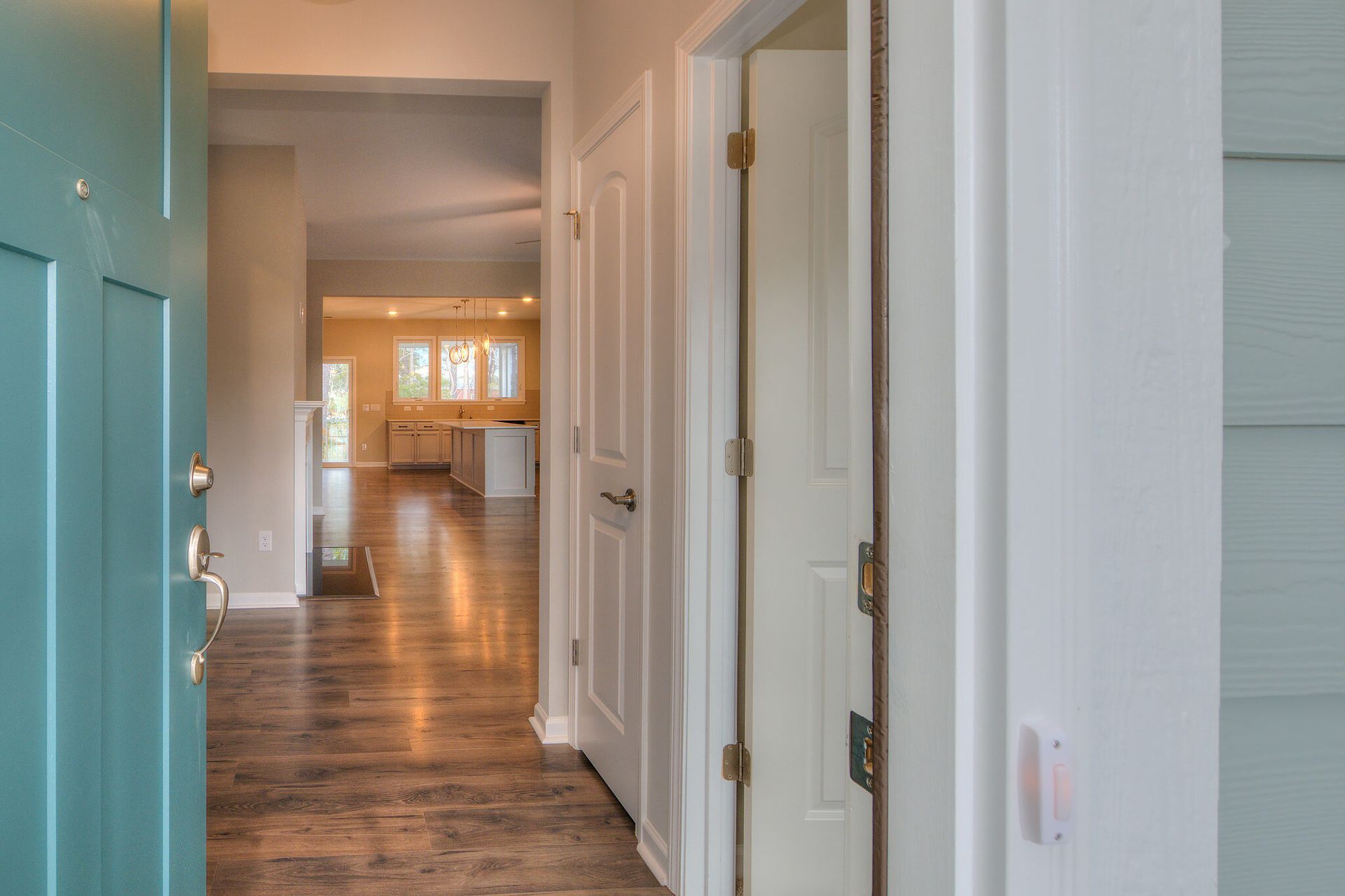 A hallway with a blue door and white doors leading to a kitchen.