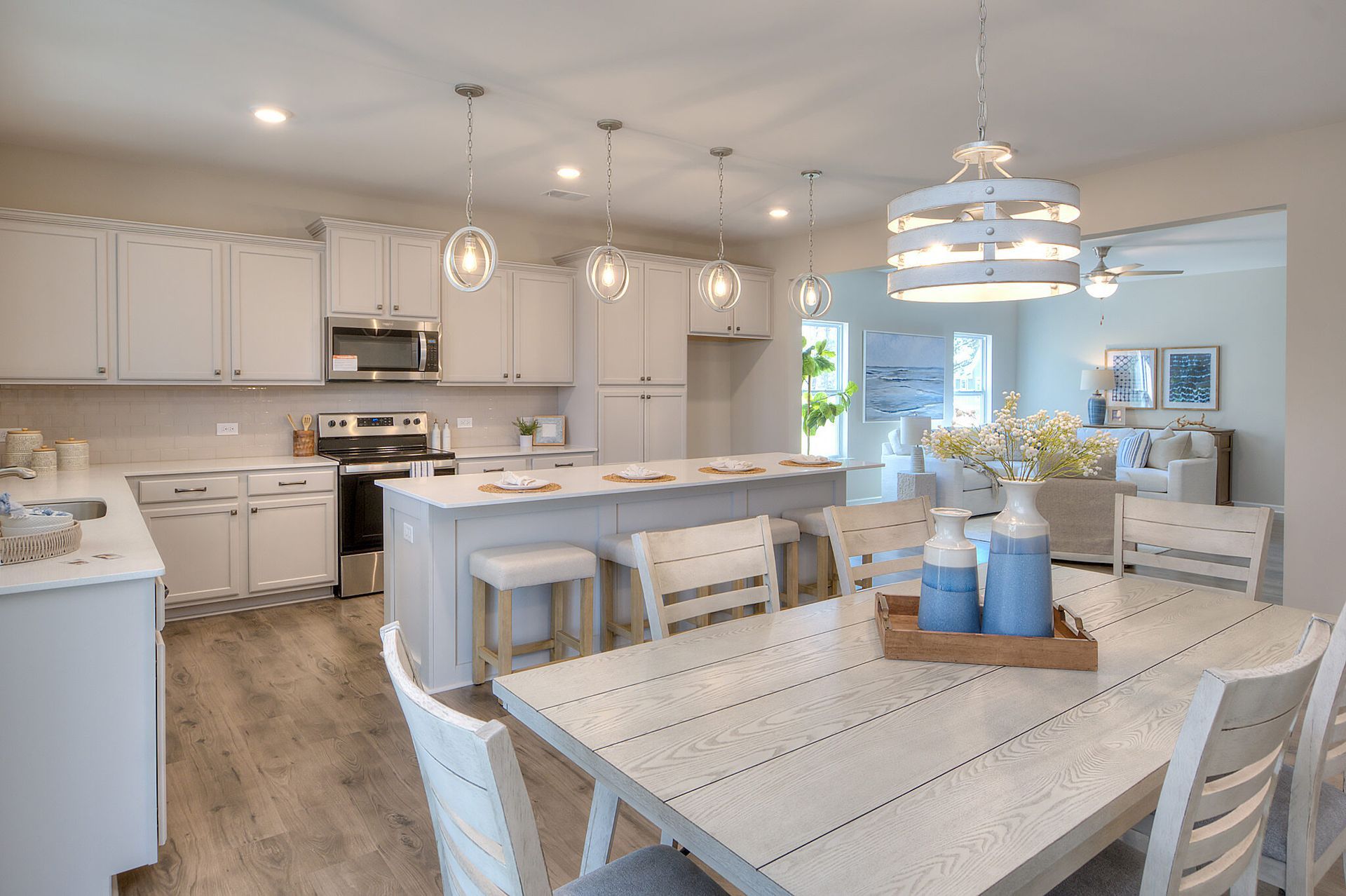 A kitchen and dining room in a model home with white cabinets and wooden floors.