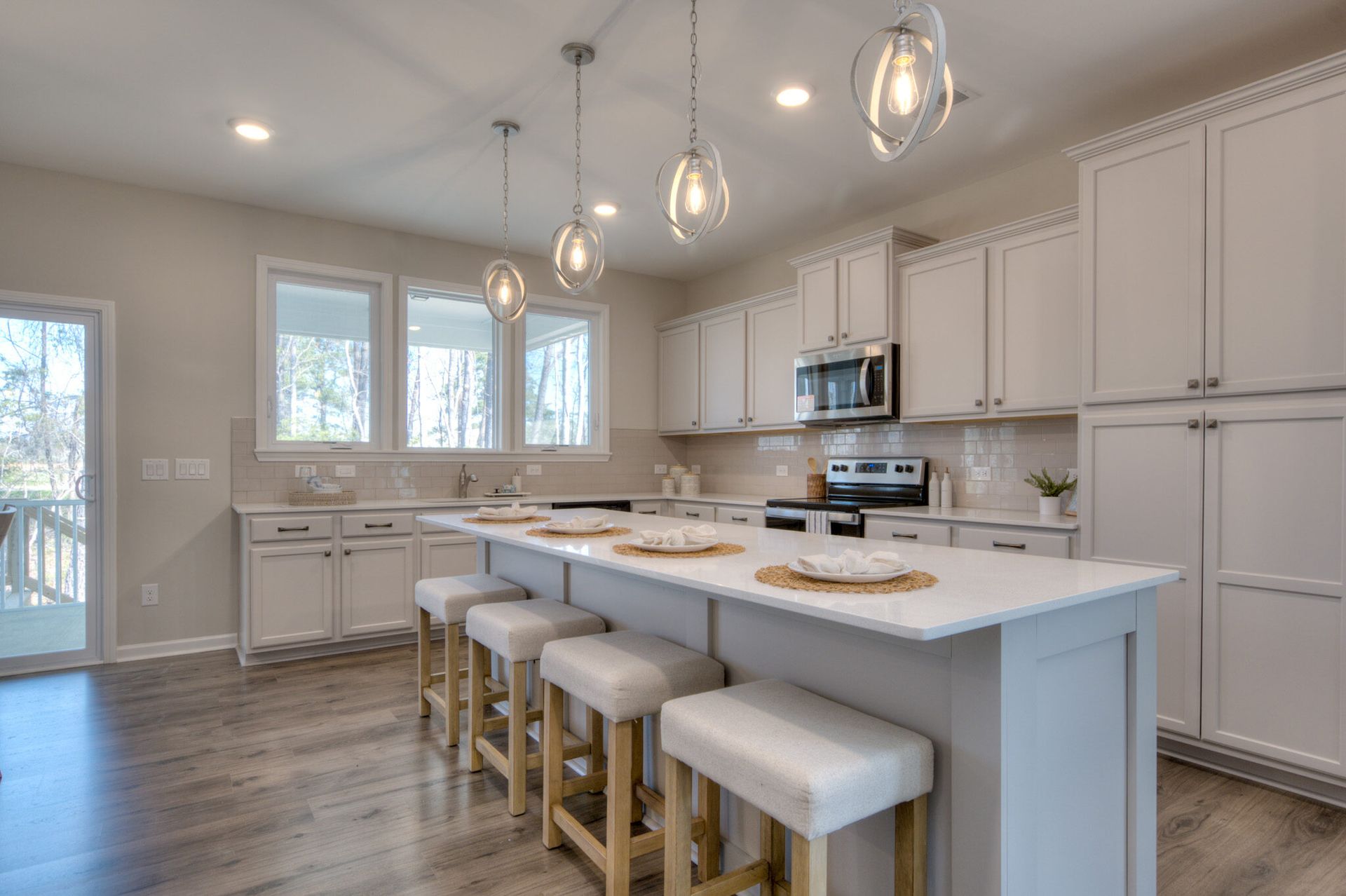 A kitchen with white cabinets , a large island , stools and a stove.