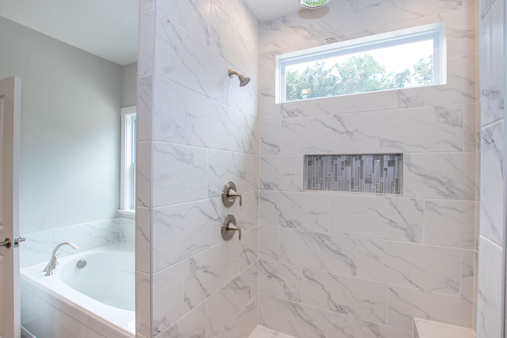 A bathroom with a tub , shower , and window.