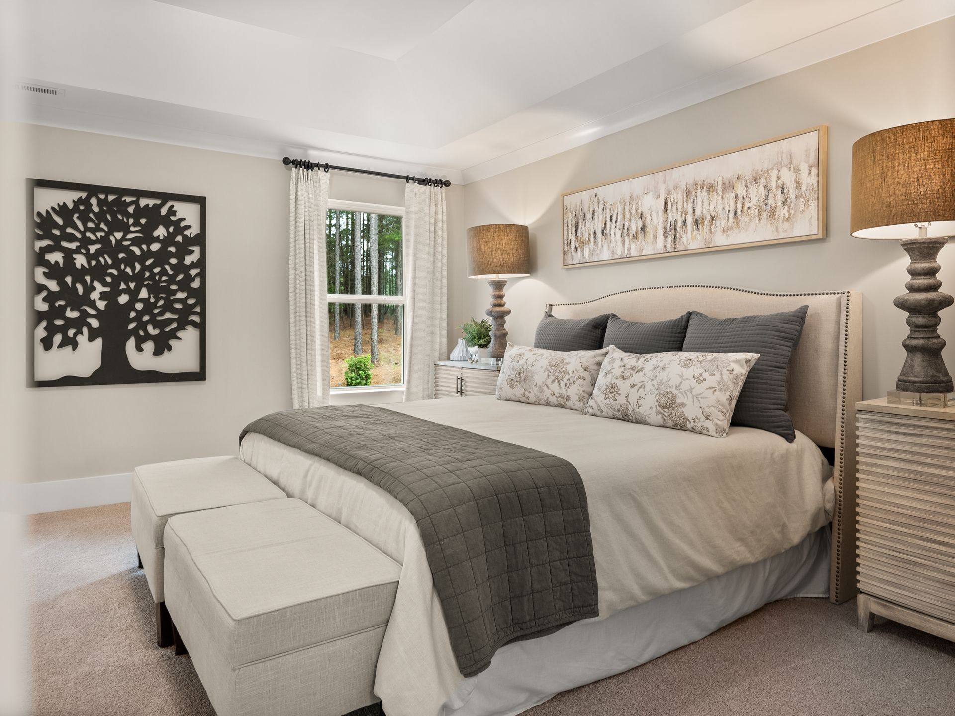 A bedroom with a king size bed , lamps , a bench and a tree on the wall.