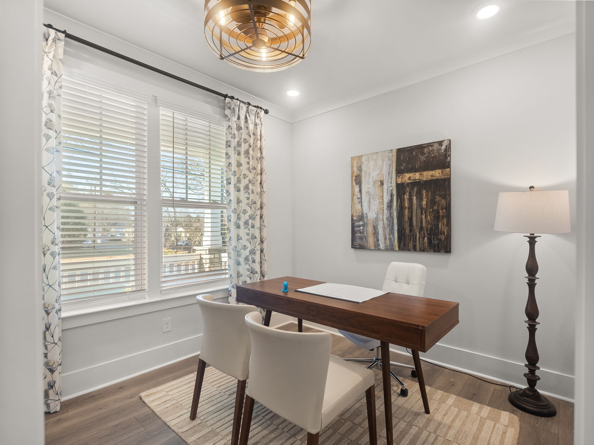 A home office with a desk , chairs and a lamp.