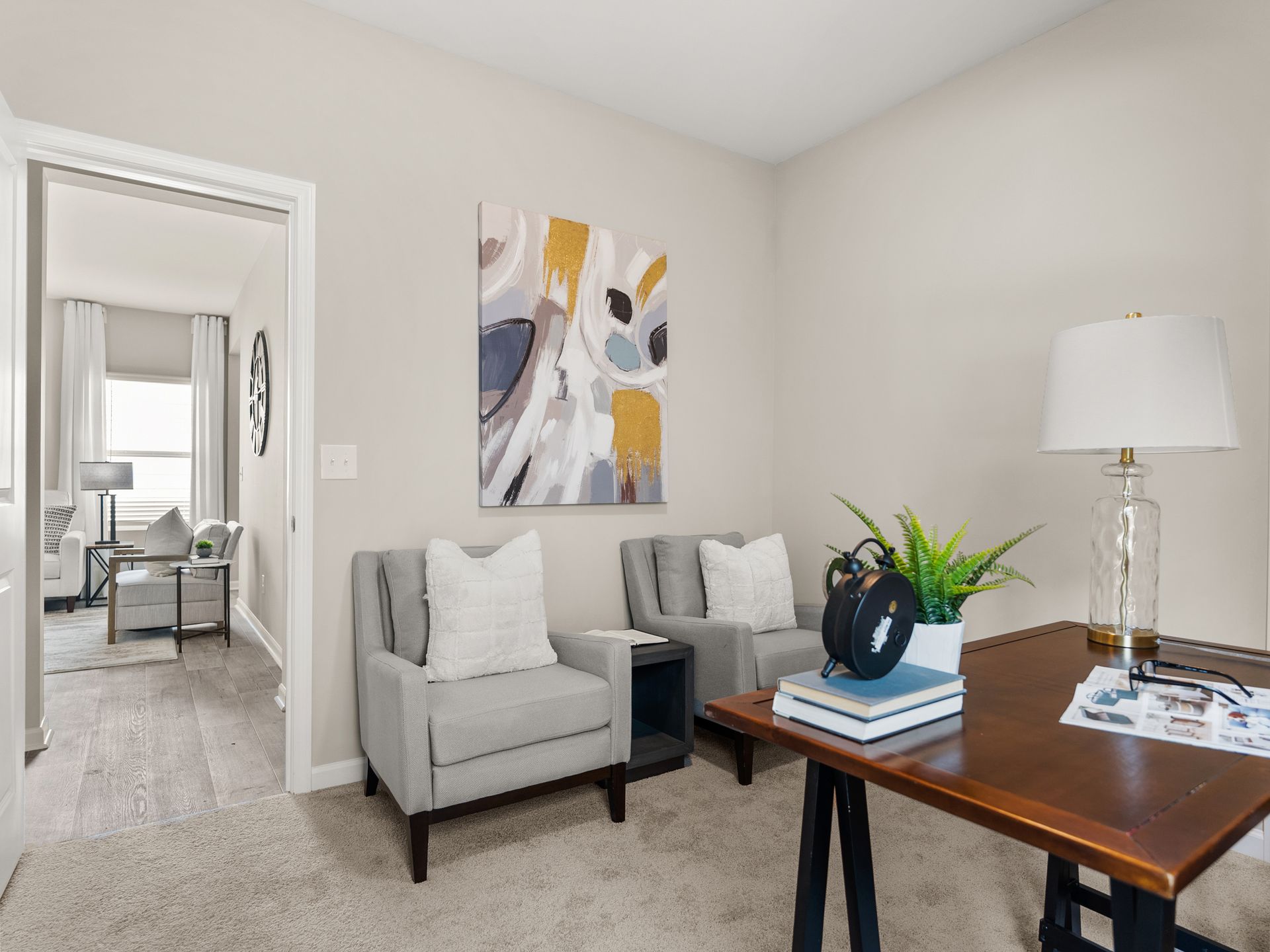 A home office with two chairs , a desk , a lamp and a painting on the wall.