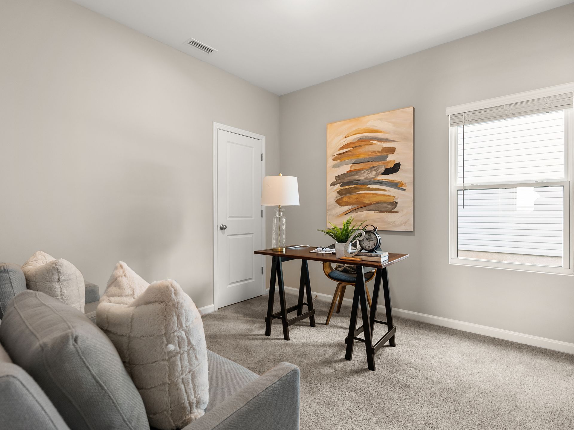 A living room with a couch , desk , lamp and window.