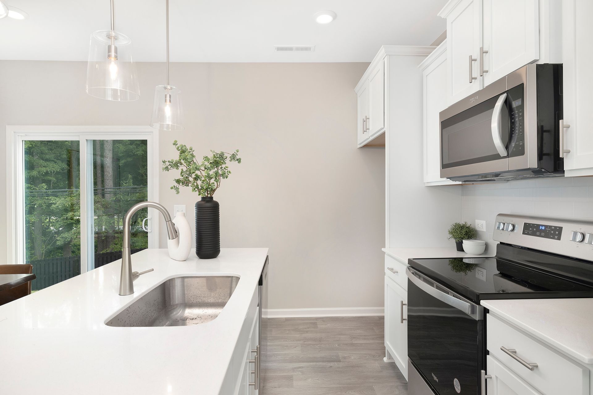 A kitchen with white cabinets , a sink , a stove , and a microwave.