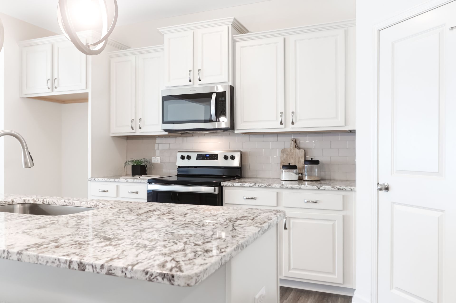 A kitchen with white cabinets , granite counter tops , a stove , microwave and sink.