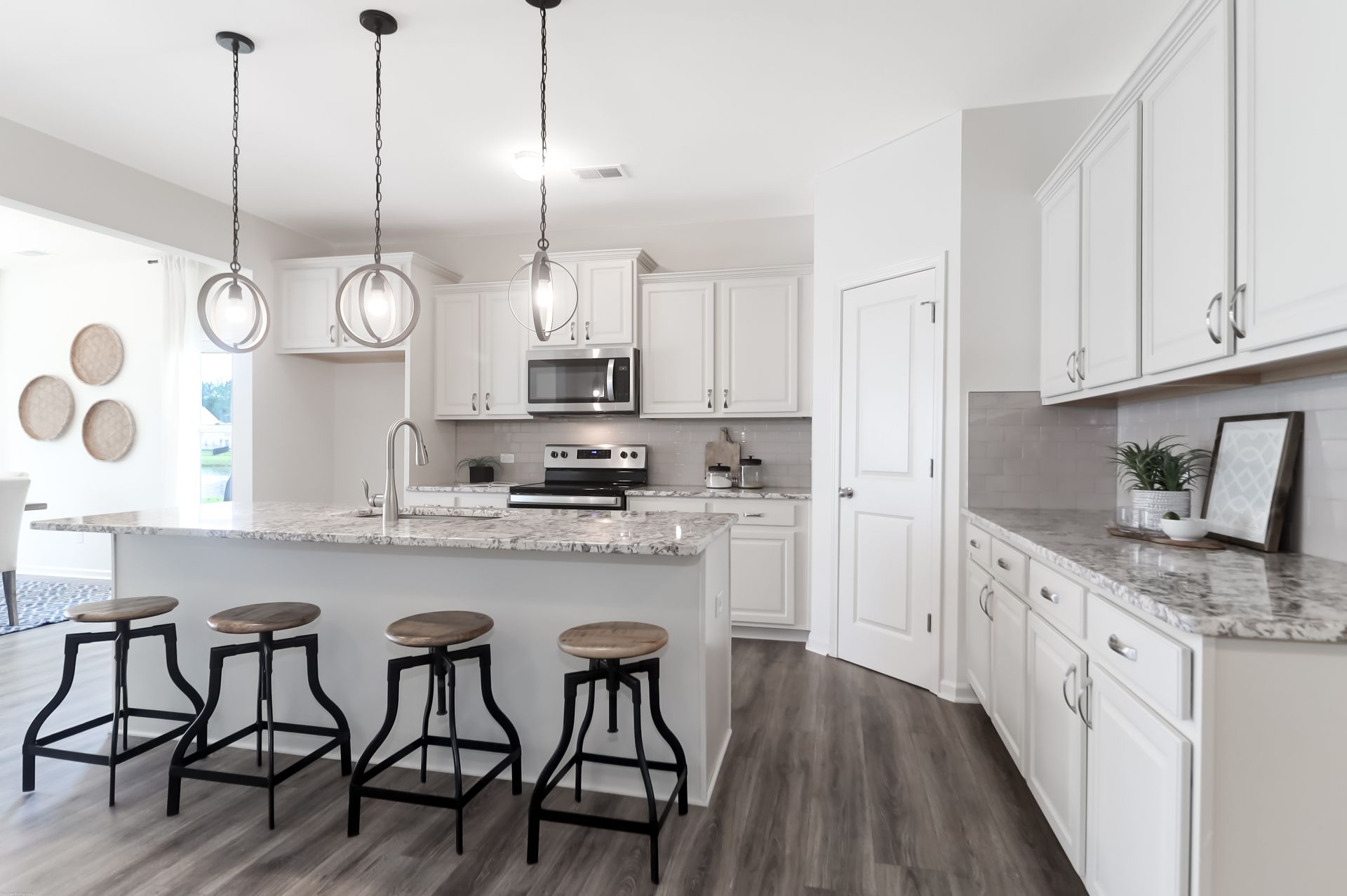 A kitchen with white cabinets , granite counter tops , stools and a large island.