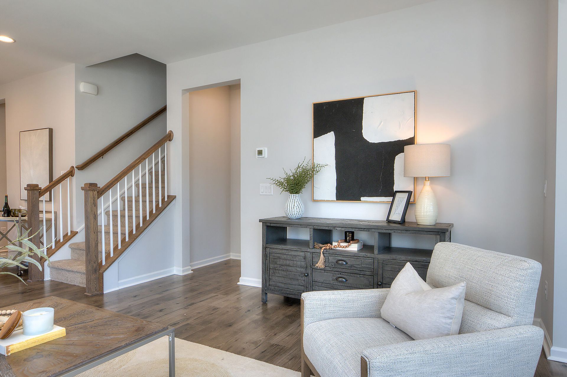 A living room with a chair , table , stairs and a painting on the wall.
