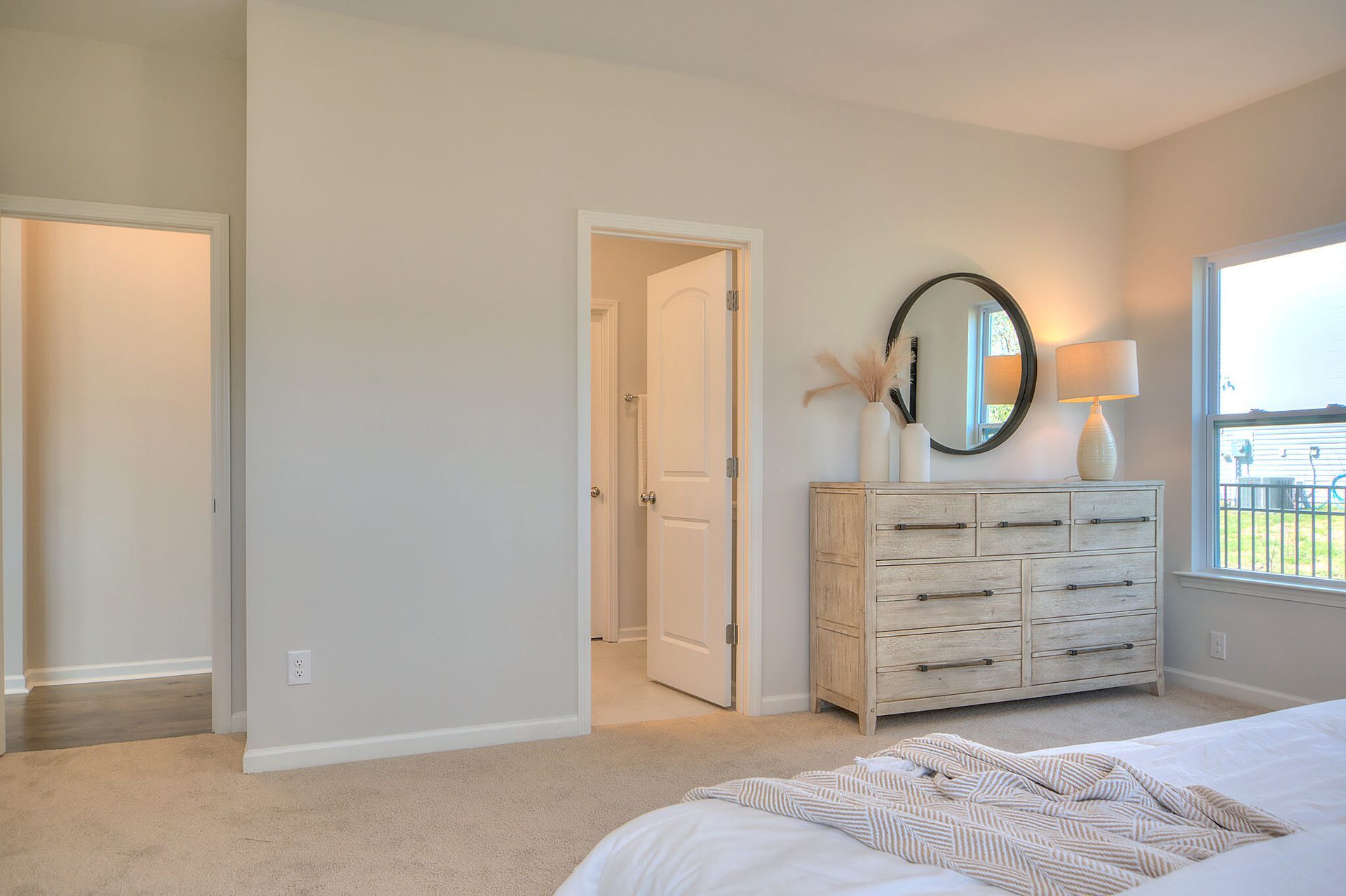 A bedroom with a bed , dresser , mirror and window.