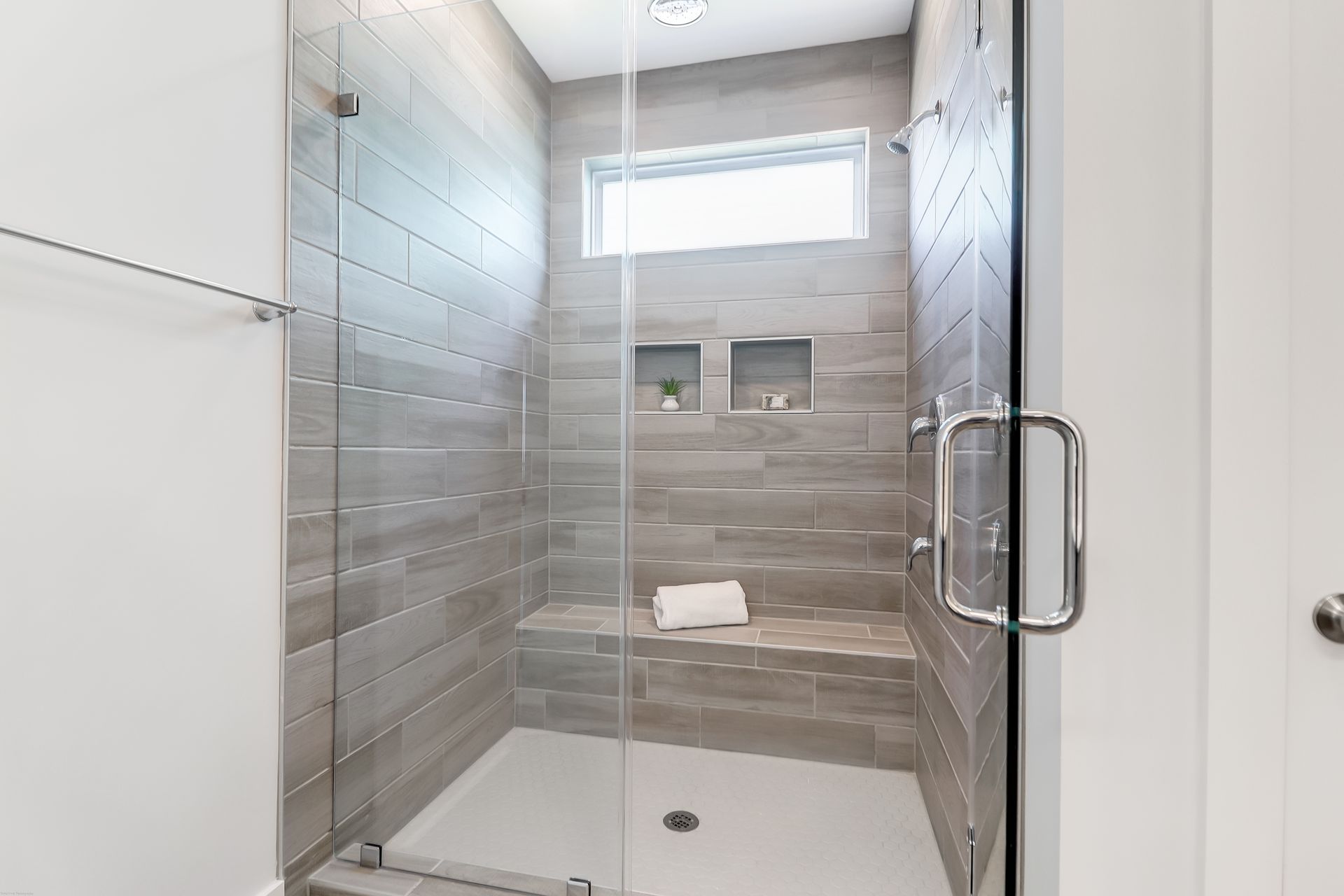 A bathroom with a walk in shower with a glass door and a window.