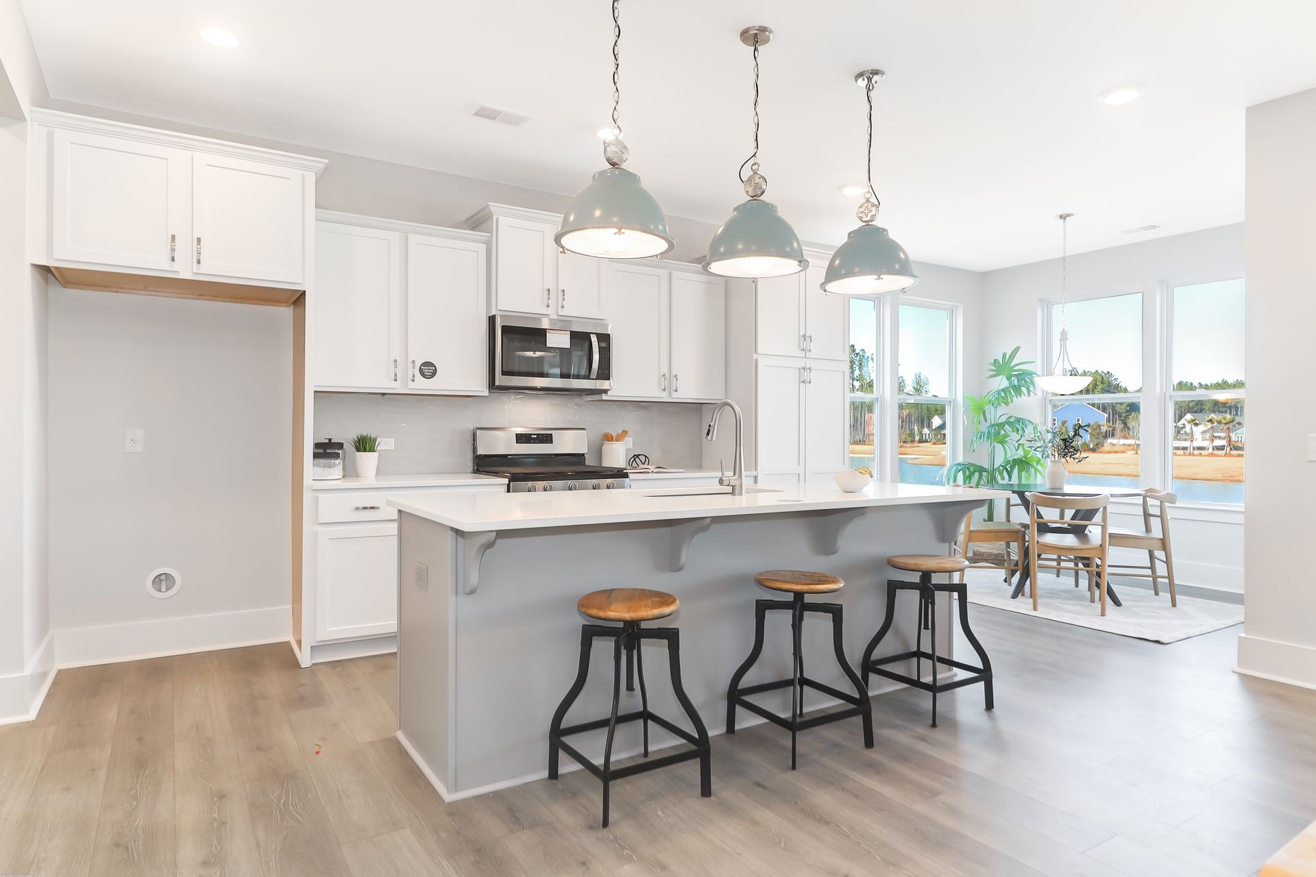 A kitchen with white cabinets , a large island , stools and a stove.