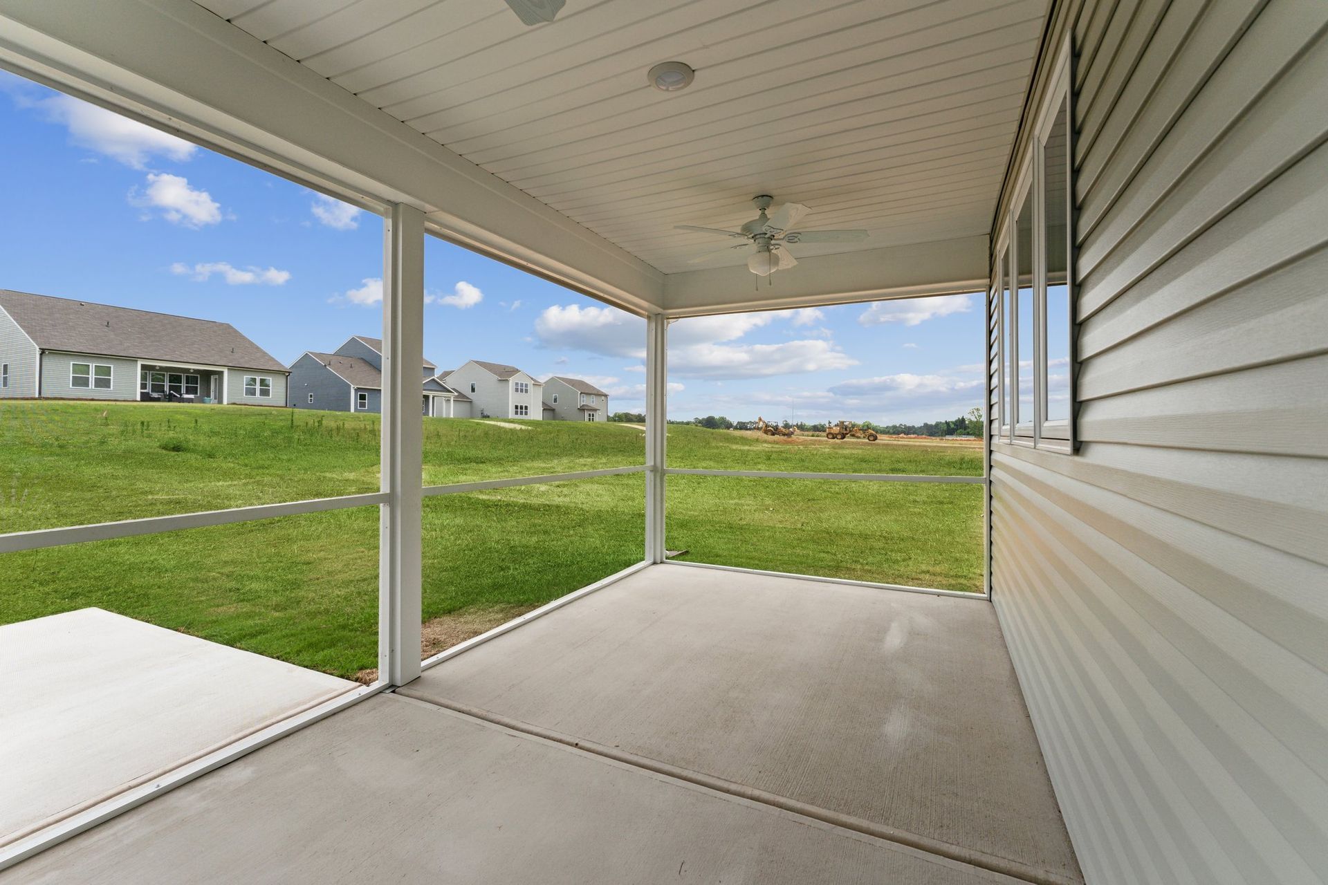 A screened in porch with a ceiling fan and a view of a grassy field.