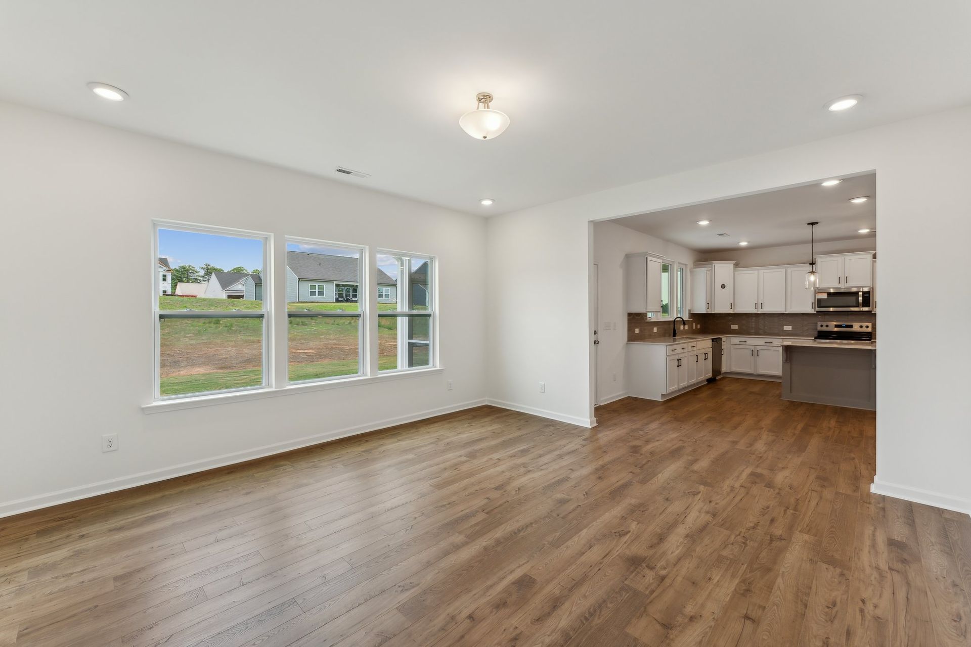 A living room with hardwood floors and a kitchen in the background.