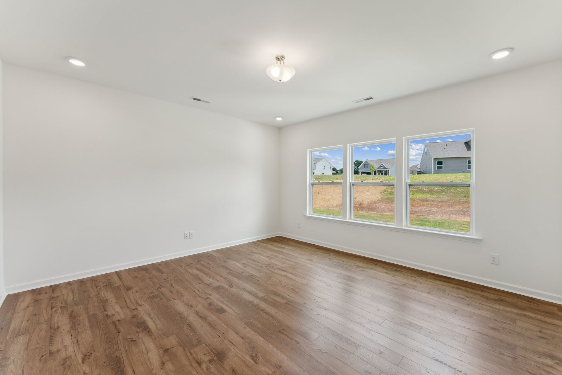 An empty room with hardwood floors and three windows.