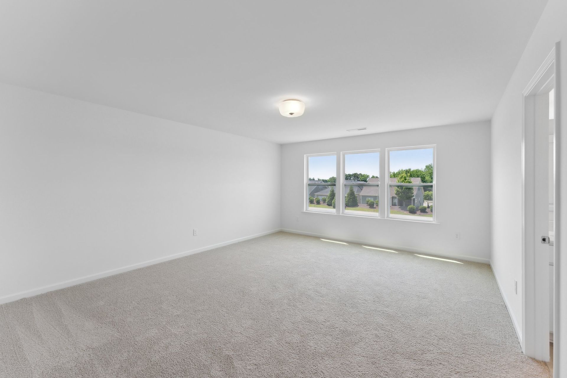 An empty bedroom with a carpeted floor and three windows.