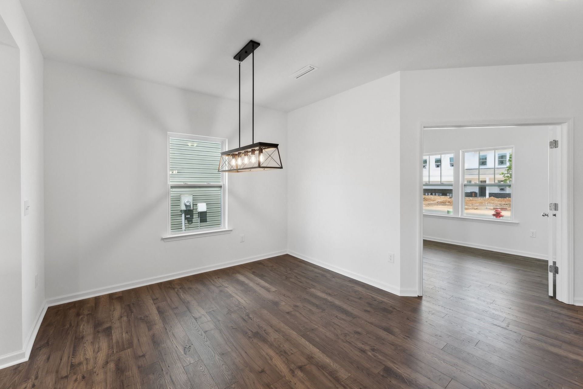 An empty dining room with hardwood floors and a chandelier hanging from the ceiling.