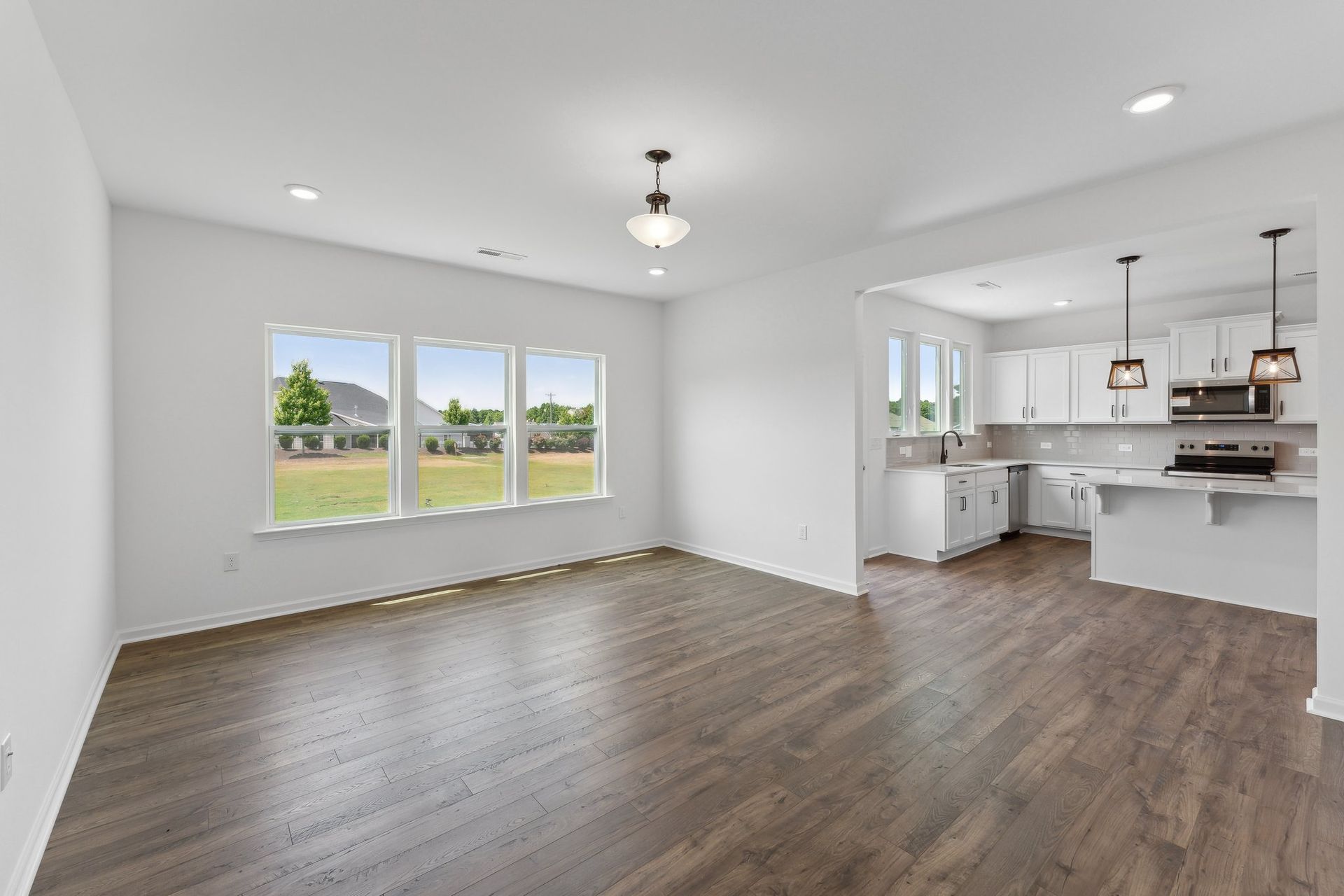 An empty living room with hardwood floors and a kitchen in the background.