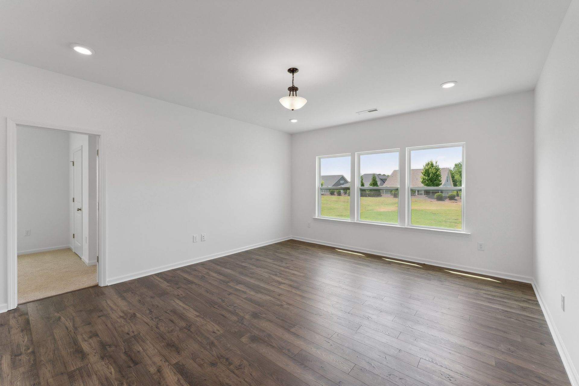 An empty living room with hardwood floors and three windows.