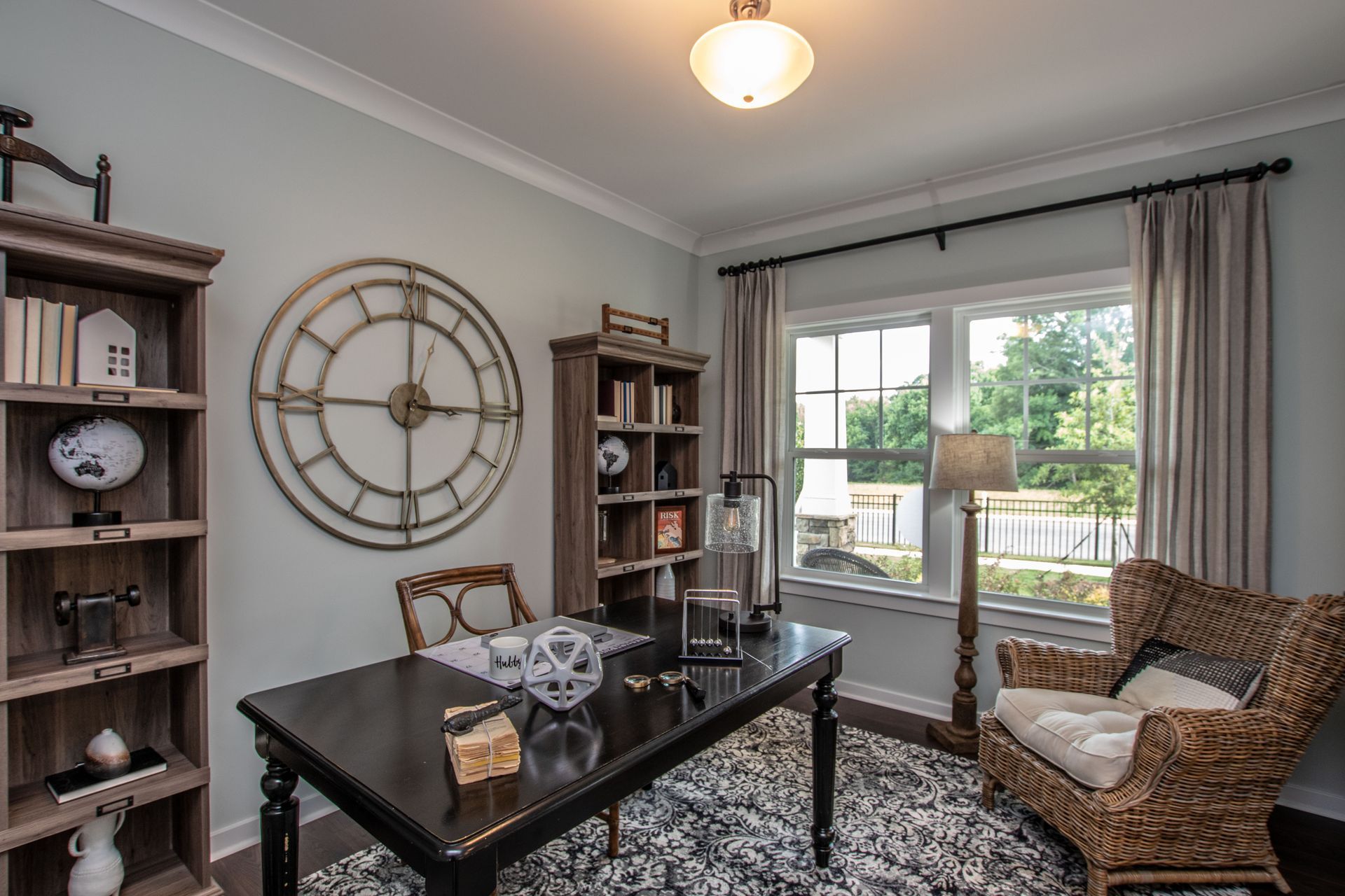 A home office with a desk , chairs , shelves and a large clock on the wall.