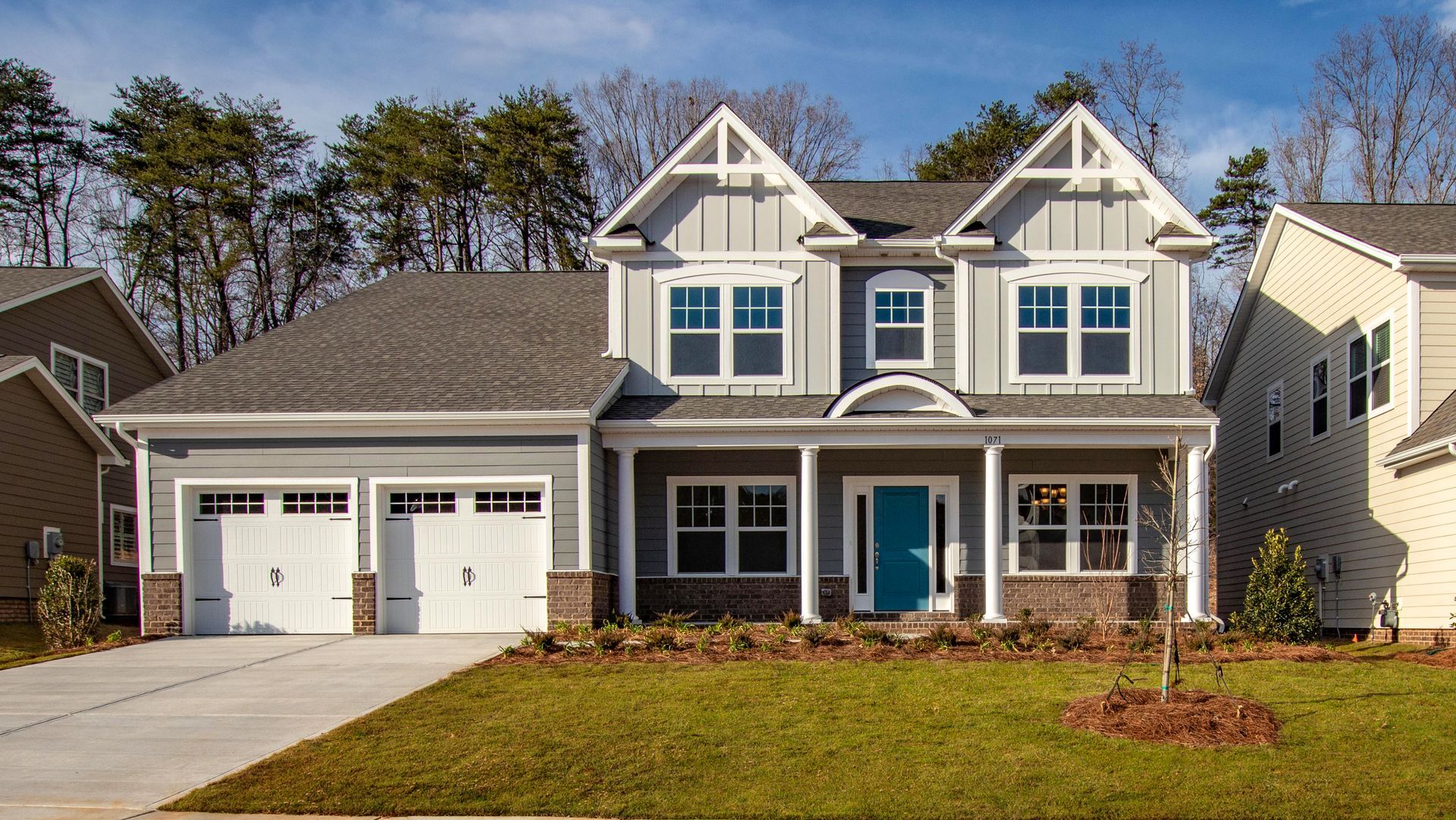 A large house with two garages and a blue door is sitting on top of a lush green lawn.