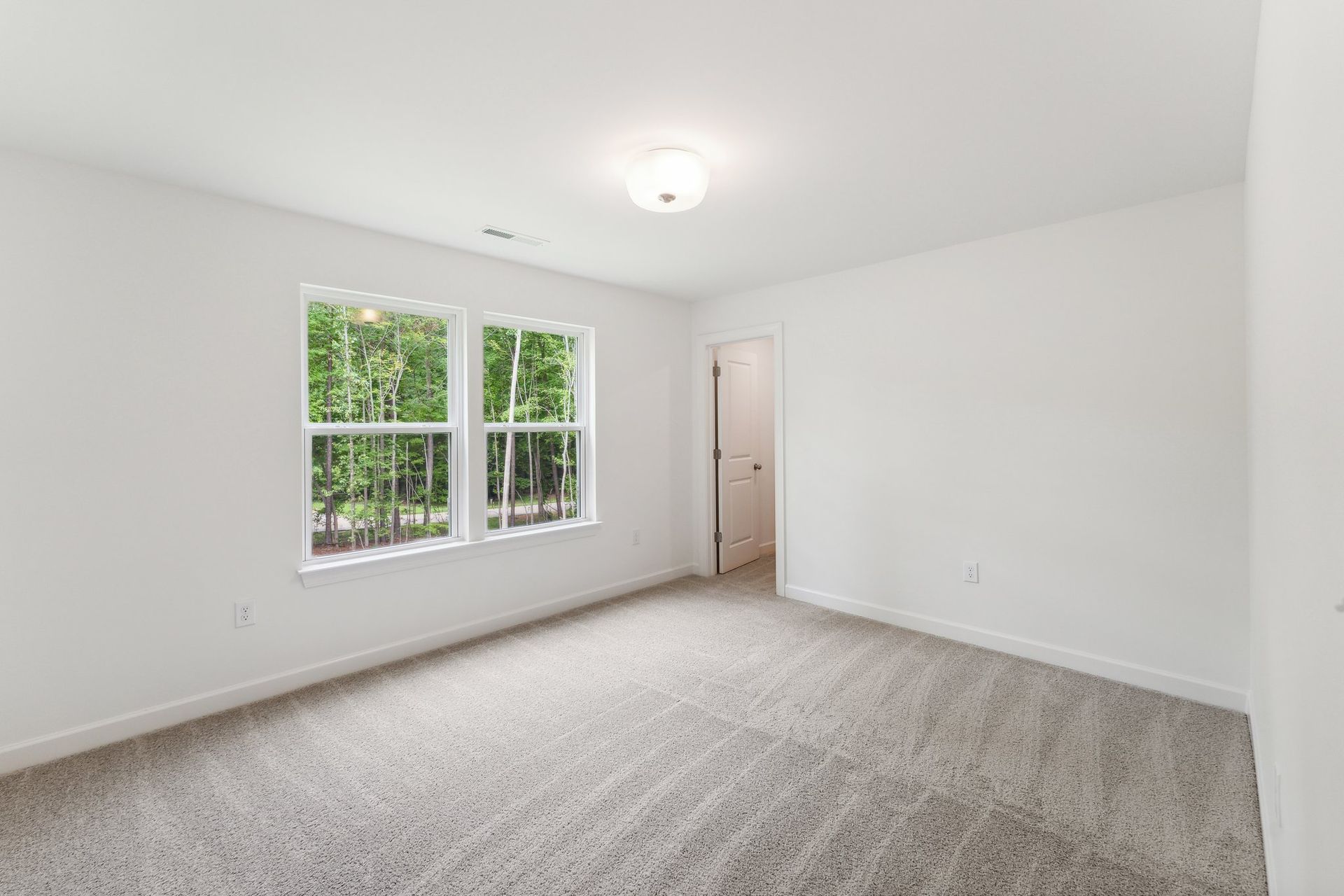 An empty bedroom with a carpeted floor and two windows.