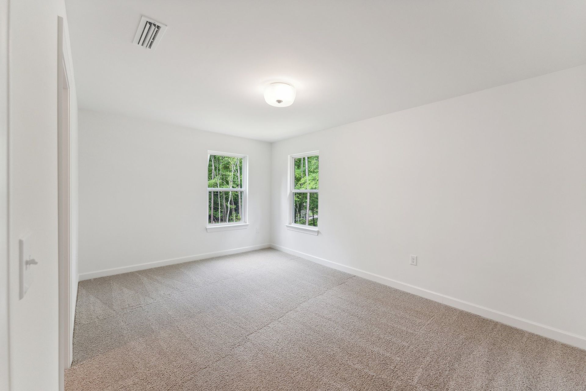 An empty bedroom with two windows and a carpeted floor.
