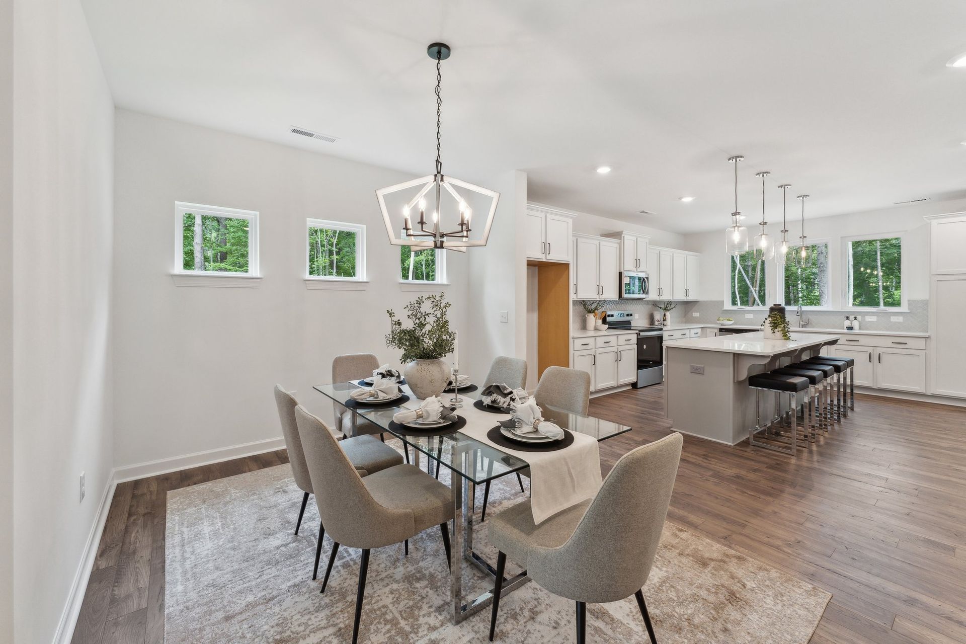 A dining room with a table and chairs and a kitchen in the background.