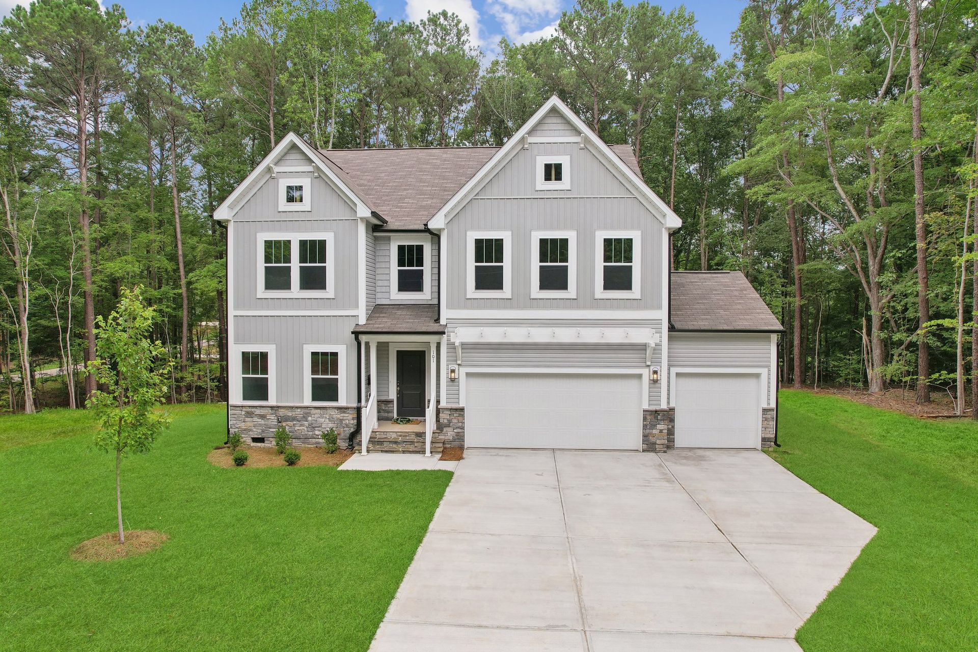 A large gray house with a driveway and trees in the background.