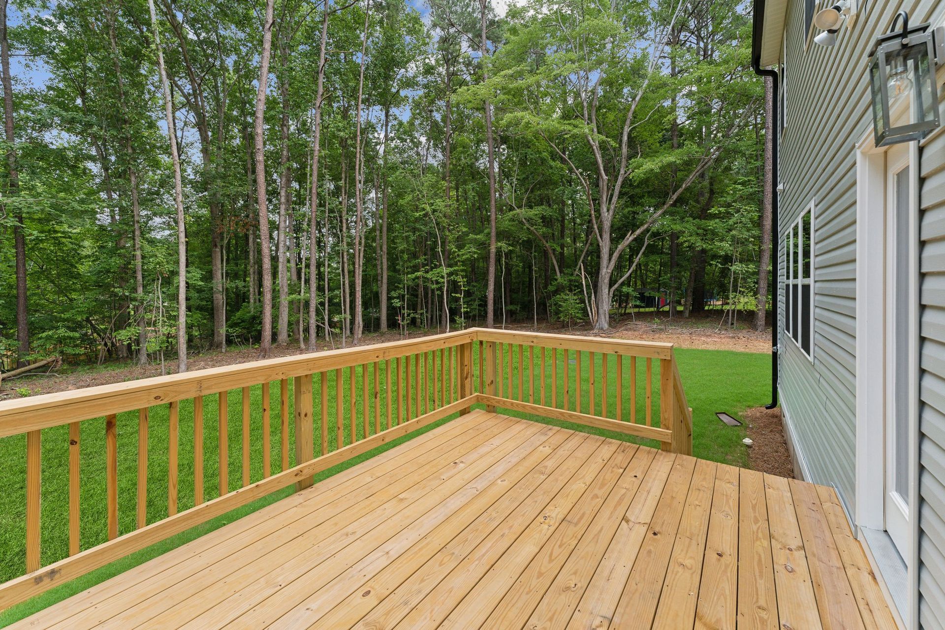 There is a large wooden deck in front of a house with trees in the background.