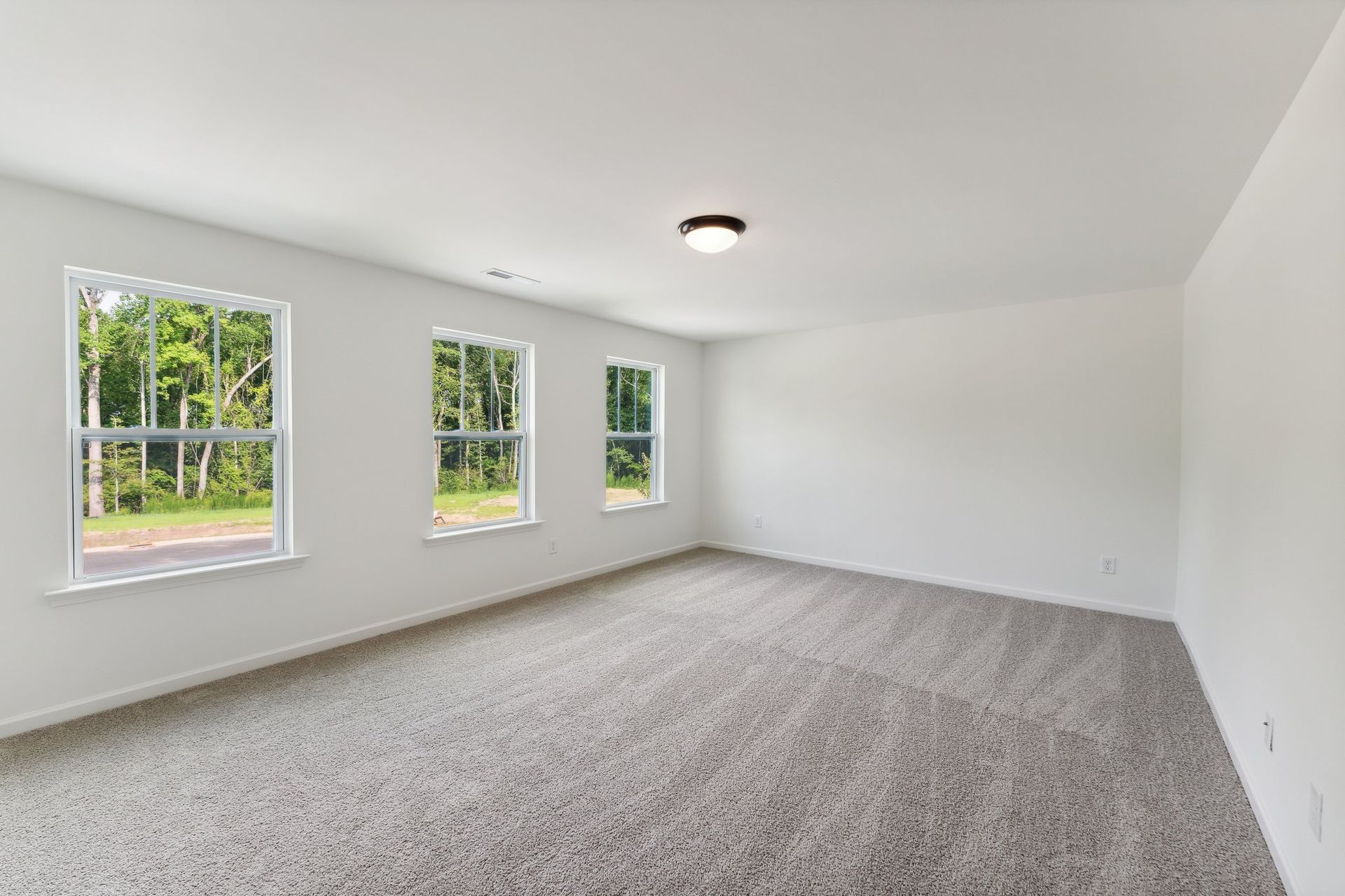 An empty room with a carpeted floor and three windows.