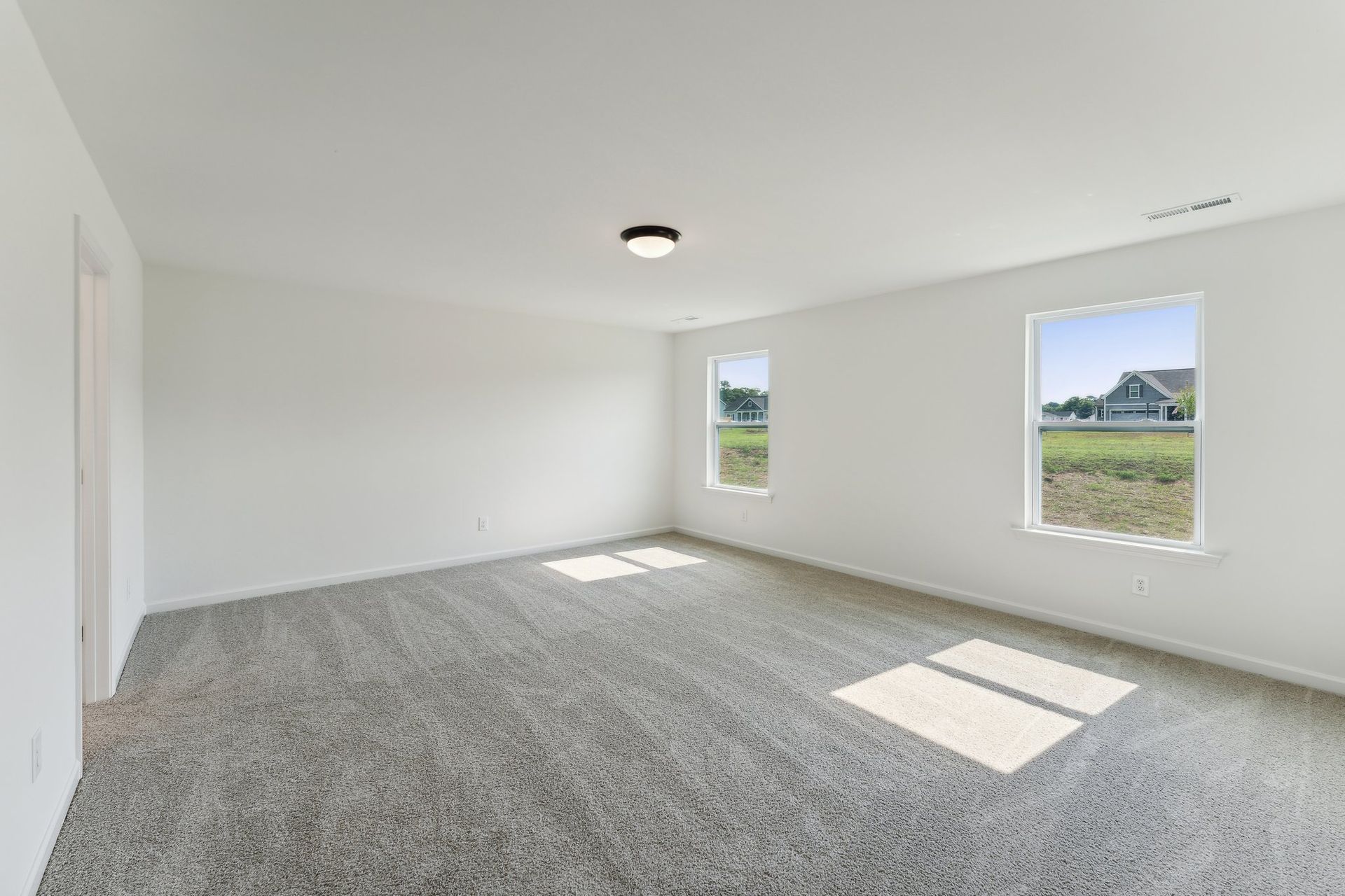 An empty room with a carpeted floor and two windows.