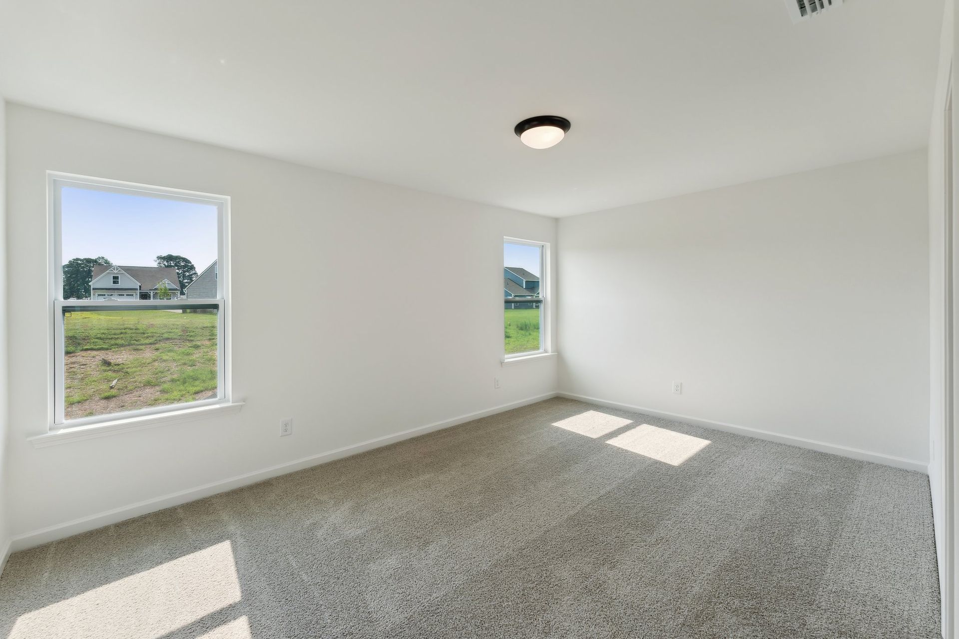 An empty bedroom with a carpeted floor and two windows.