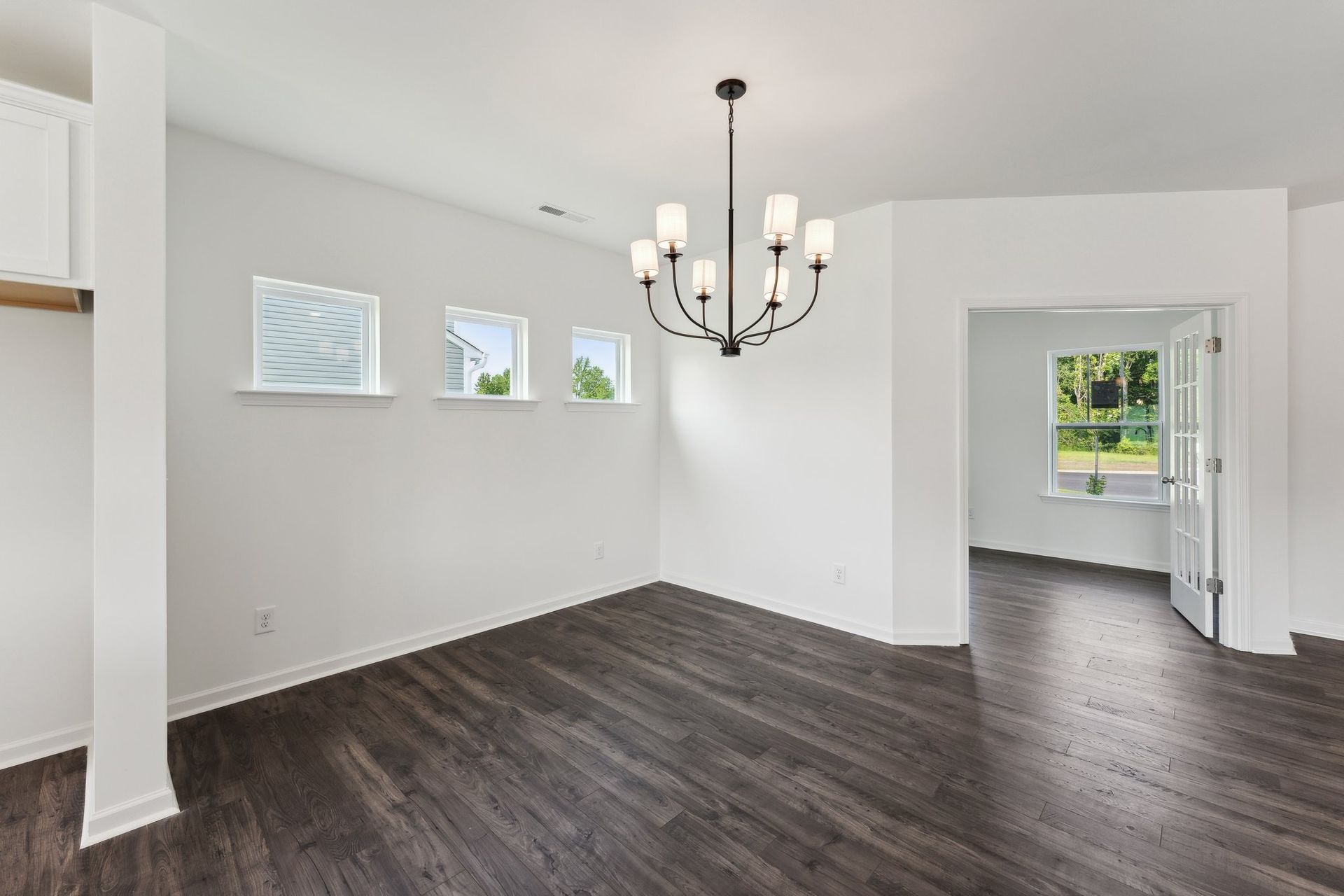 An empty dining room with hardwood floors and a chandelier.