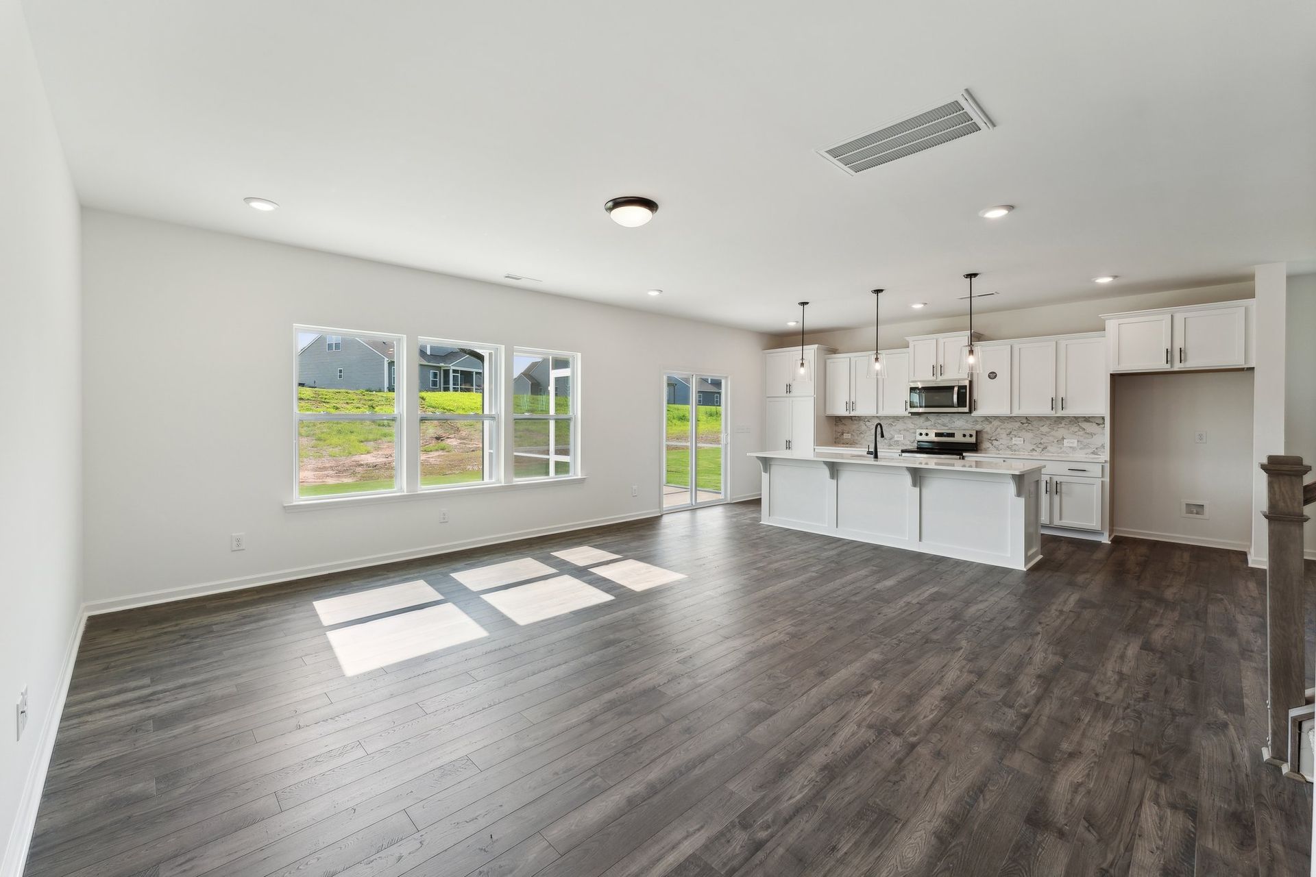 A living room with hardwood floors and a kitchen in a new home.