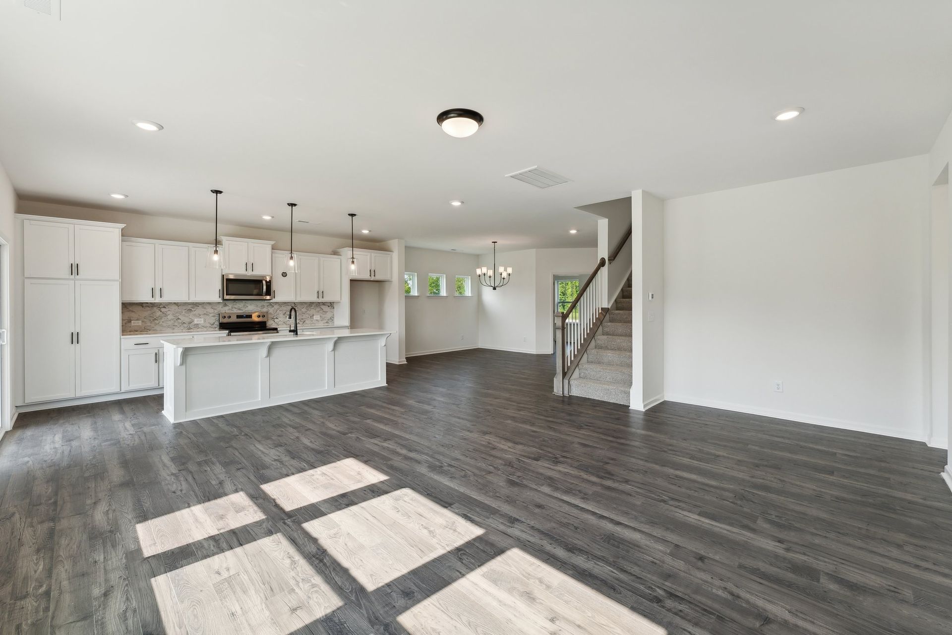 A large empty room with a kitchen and stairs.