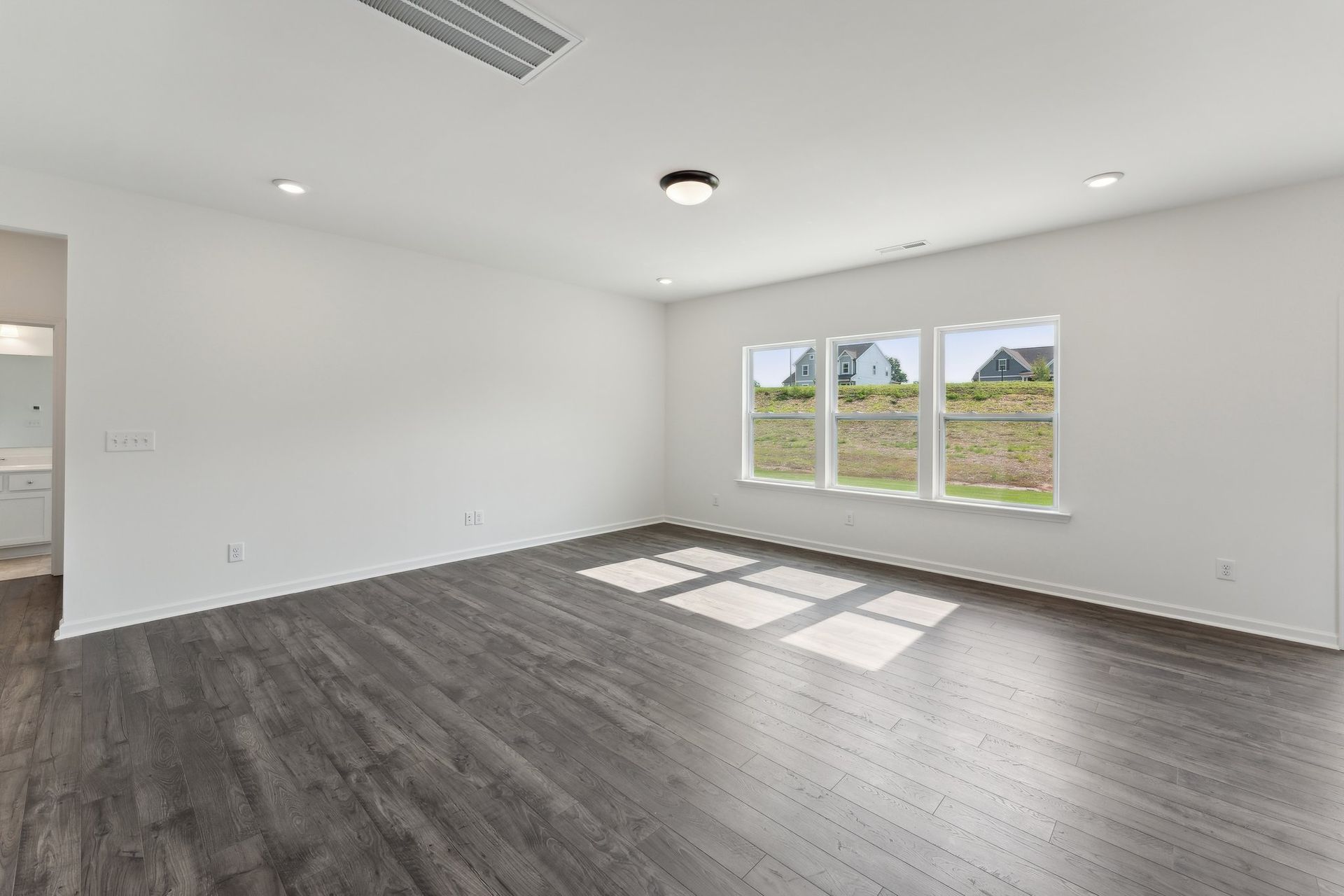 An empty living room with hardwood floors and three windows.