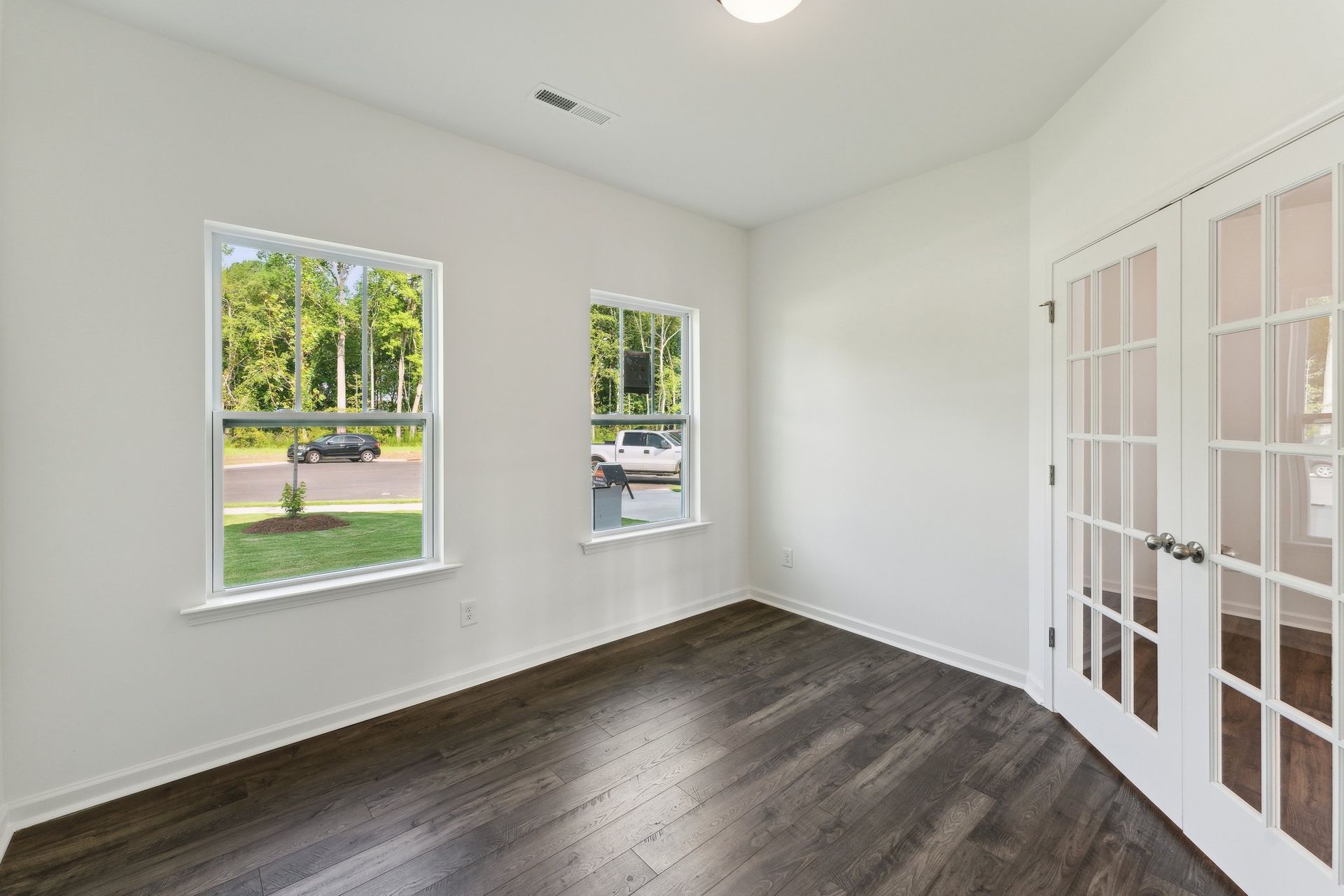 An empty room with hardwood floors and two windows.